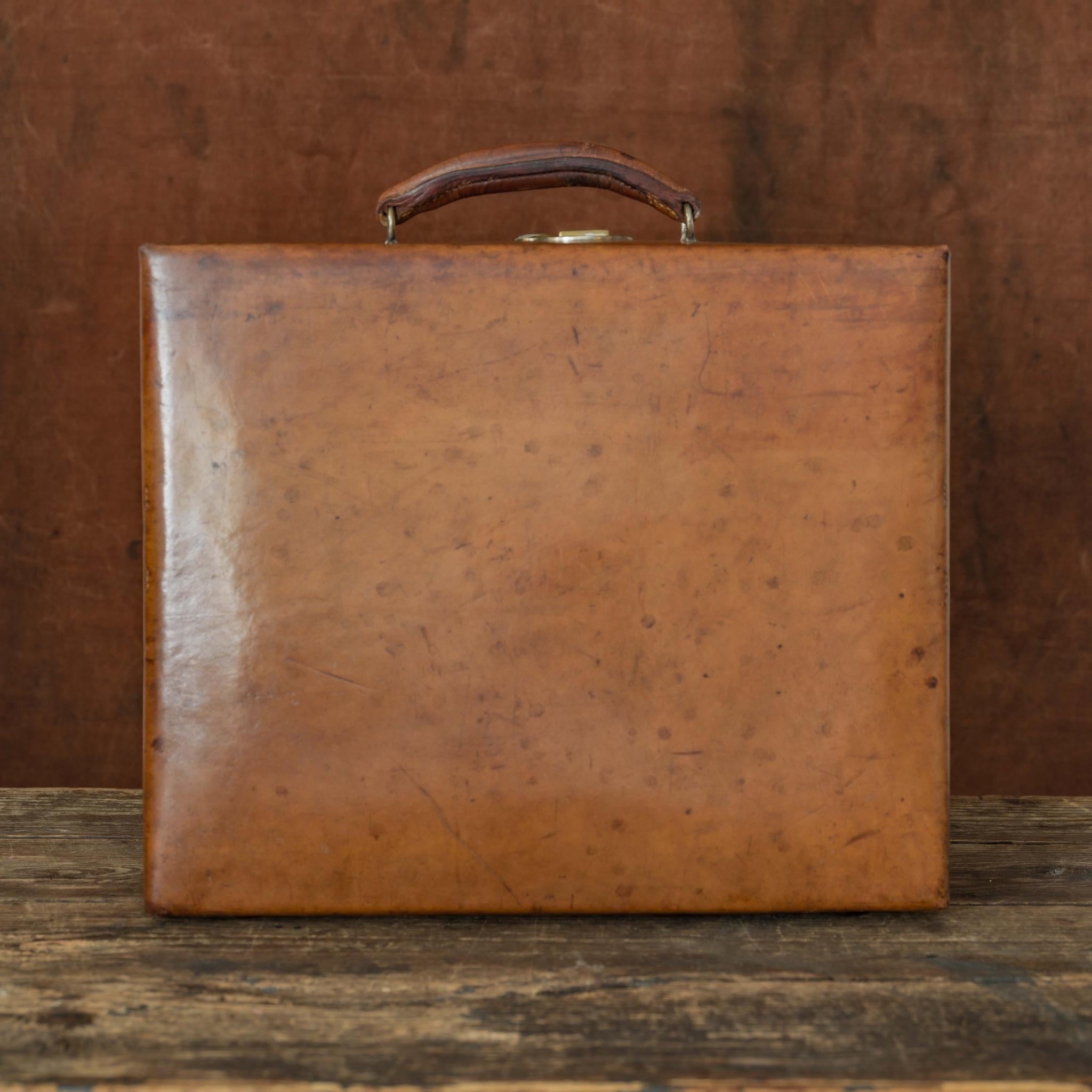 An excellent sturdy tan leather case with solid brass catch and original leather lining with pockets and sleeves to accommodate fittings (now missing). The fittings that remain are the blotter folder, the ink pot and matching vesta case. Circa
