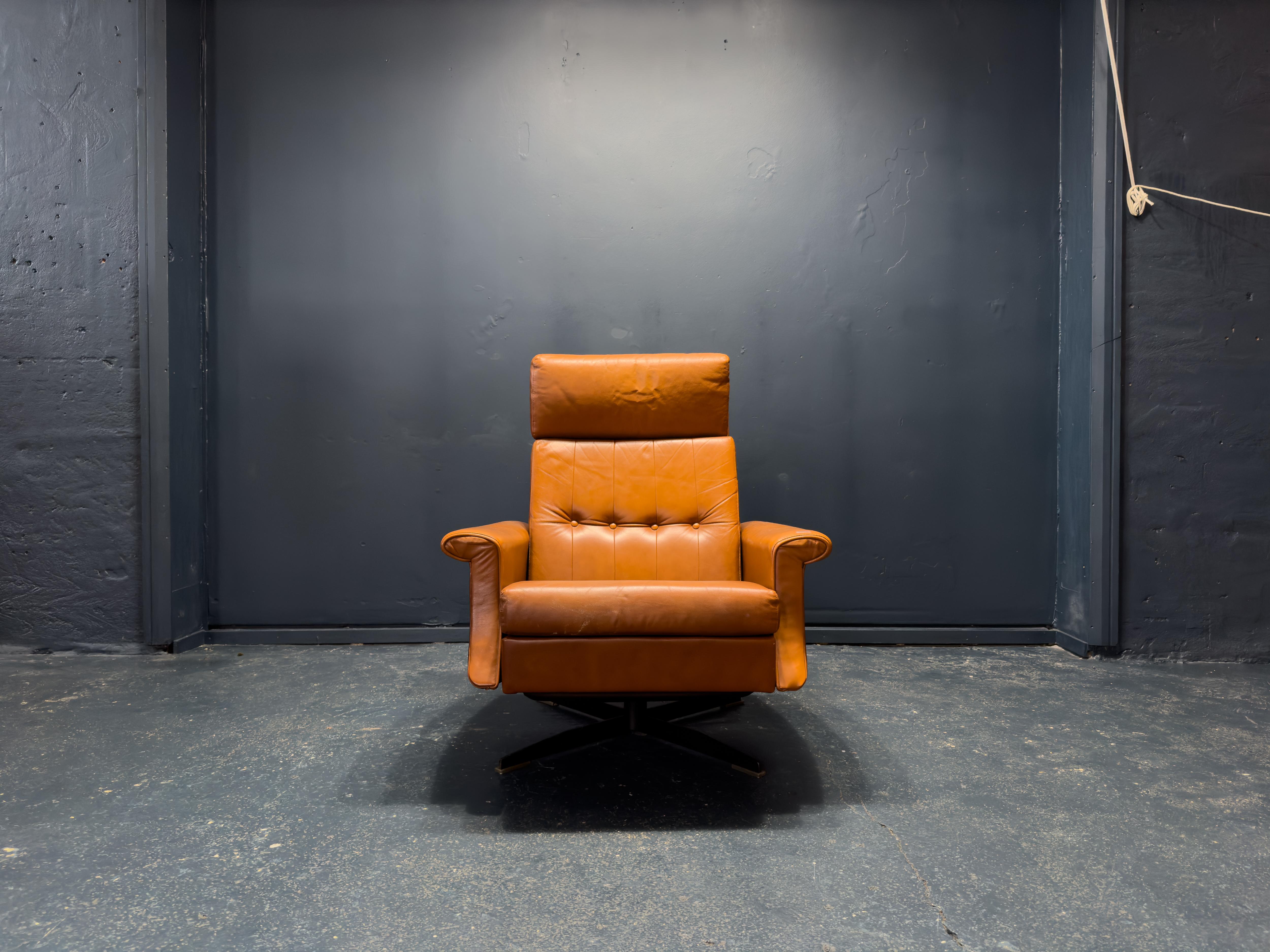 This vintage leather reclining chair exudes both sophistication and comfort, making it a timeless statement piece. Upholstered in rich, cognac-toned leather, the material has a warm, inviting patina that enhances its vintage charm. The high