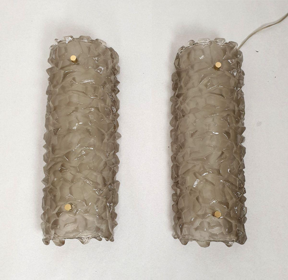 Pair of Mid Century Modern Murano glass sconces, Mazzega style, Italy 1980s.
The pair of sconces is made of a thick piece of tan/taupe Murano glass, with an irregular surface.
The Murano glass is translucent.
The back plate is painted white and the
