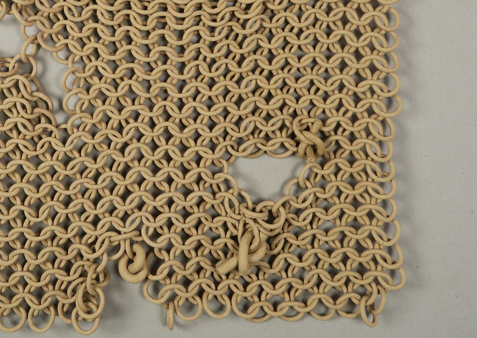 This wall sculpture balances the strength and delicacy of its materiality through the lush draping of seemingly fragile ceramic links. Each link is individually assembled into a vast weaving of ceramic rings that allows the piece to drape, fold, and
