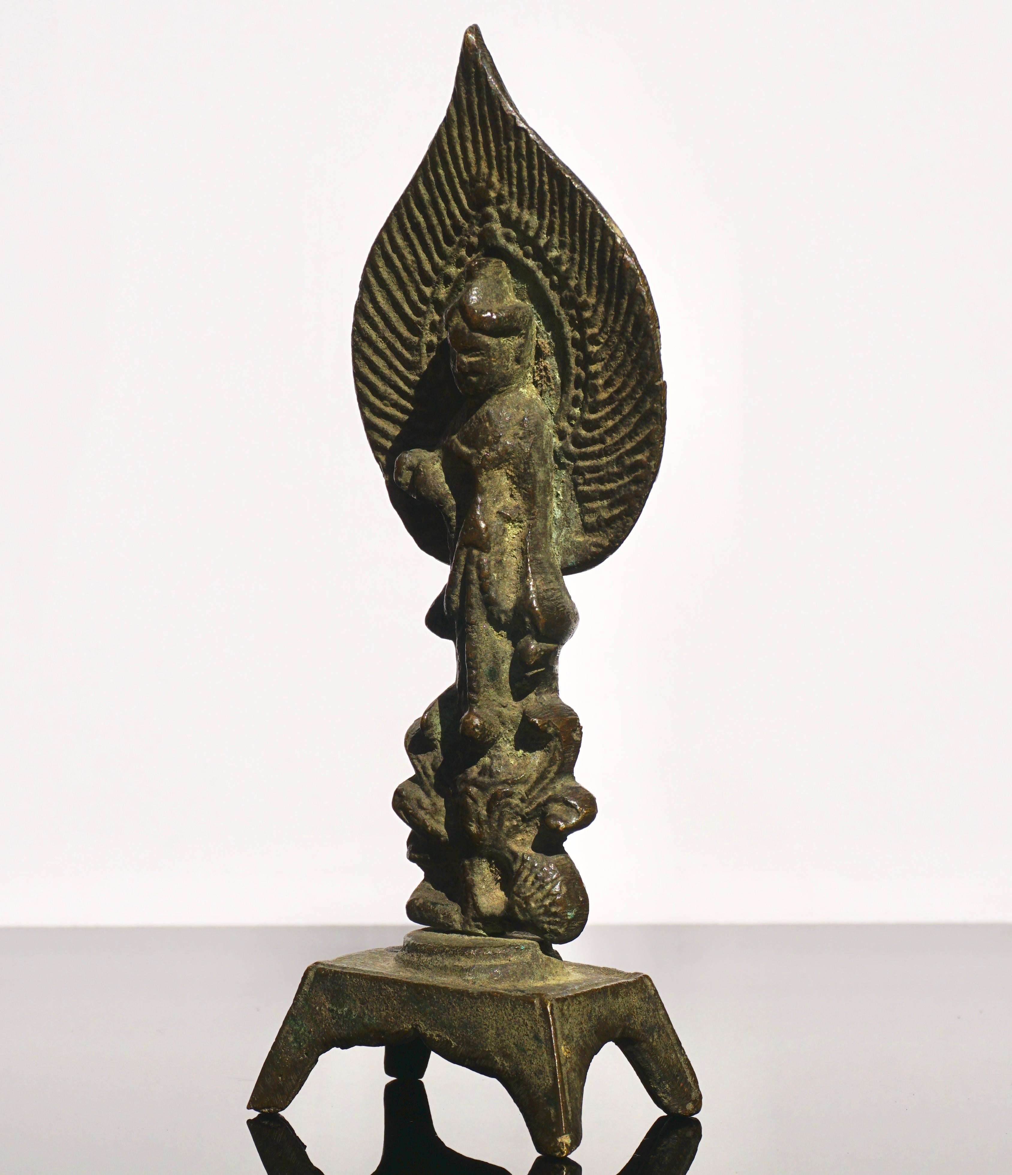 The figure is shown standing on a raised four legged base, the left hand raised in Mudra. The figure is wearing simple, diaphanous robes, and the head is framed by the flame-form mandorla which is surmounted by the standing figure of Amitabha