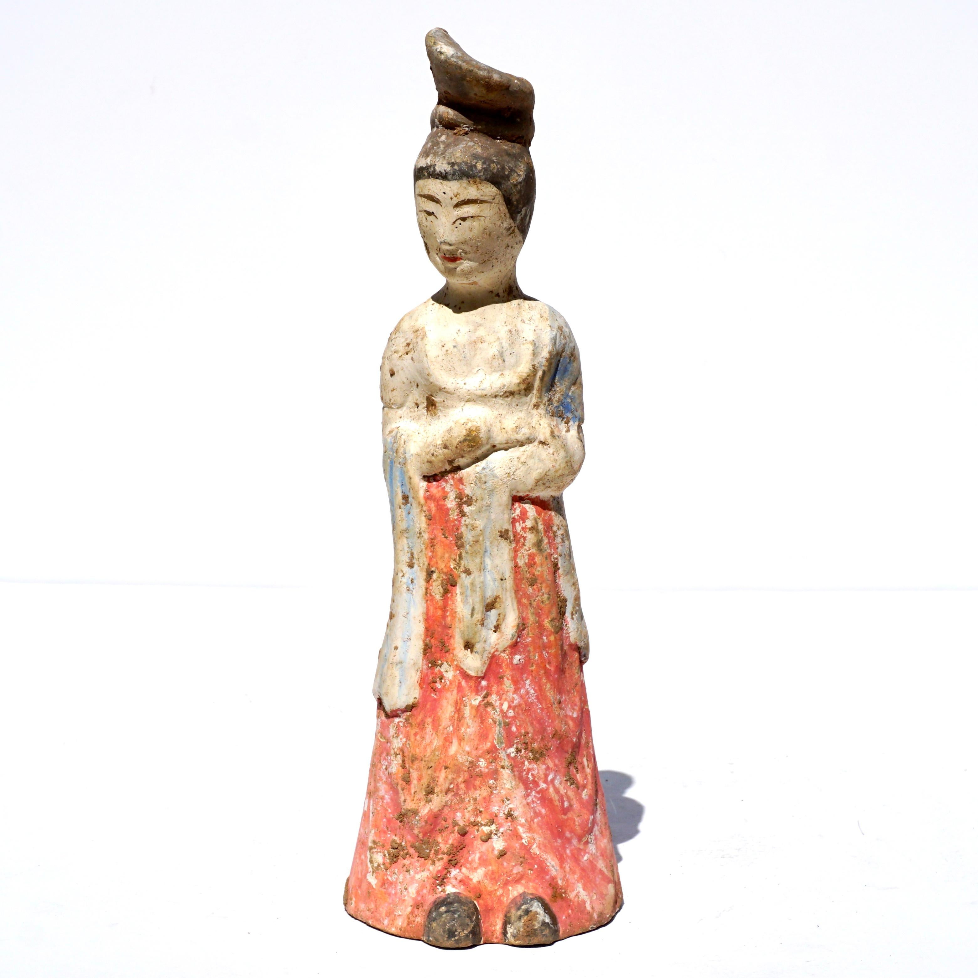 Circa (618-907 AD) A pottery tomb attendant figure in the form of a woman who is wearing a lengthy robe with a red-painted skirt, her robes are painted in beautiful blue pigment, holds her arms together against her chest and displays her smiling