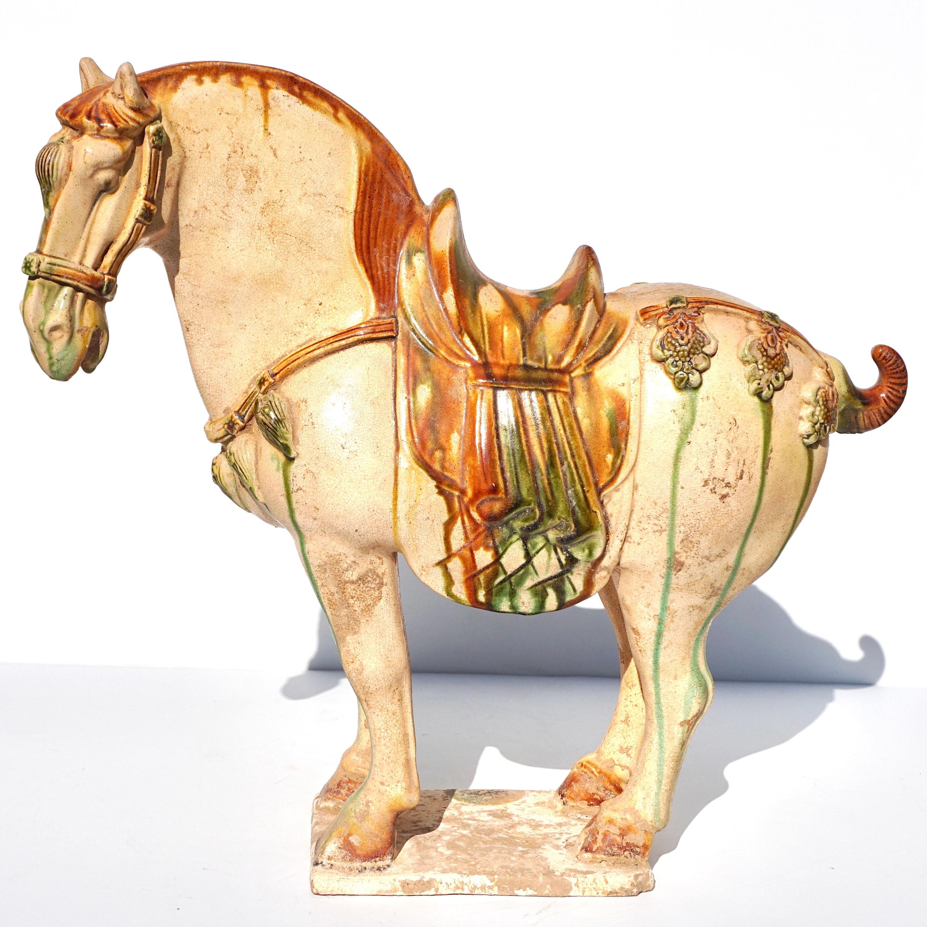 Tang Dynasty (618 - 907) Sancai glazed pottery horse

The cream-glazed horse is naturalistically modelled standing on a rectangular base, with the mane, tail and hooves highlighted in amber glaze. The head is gracefully curved to the left, with a