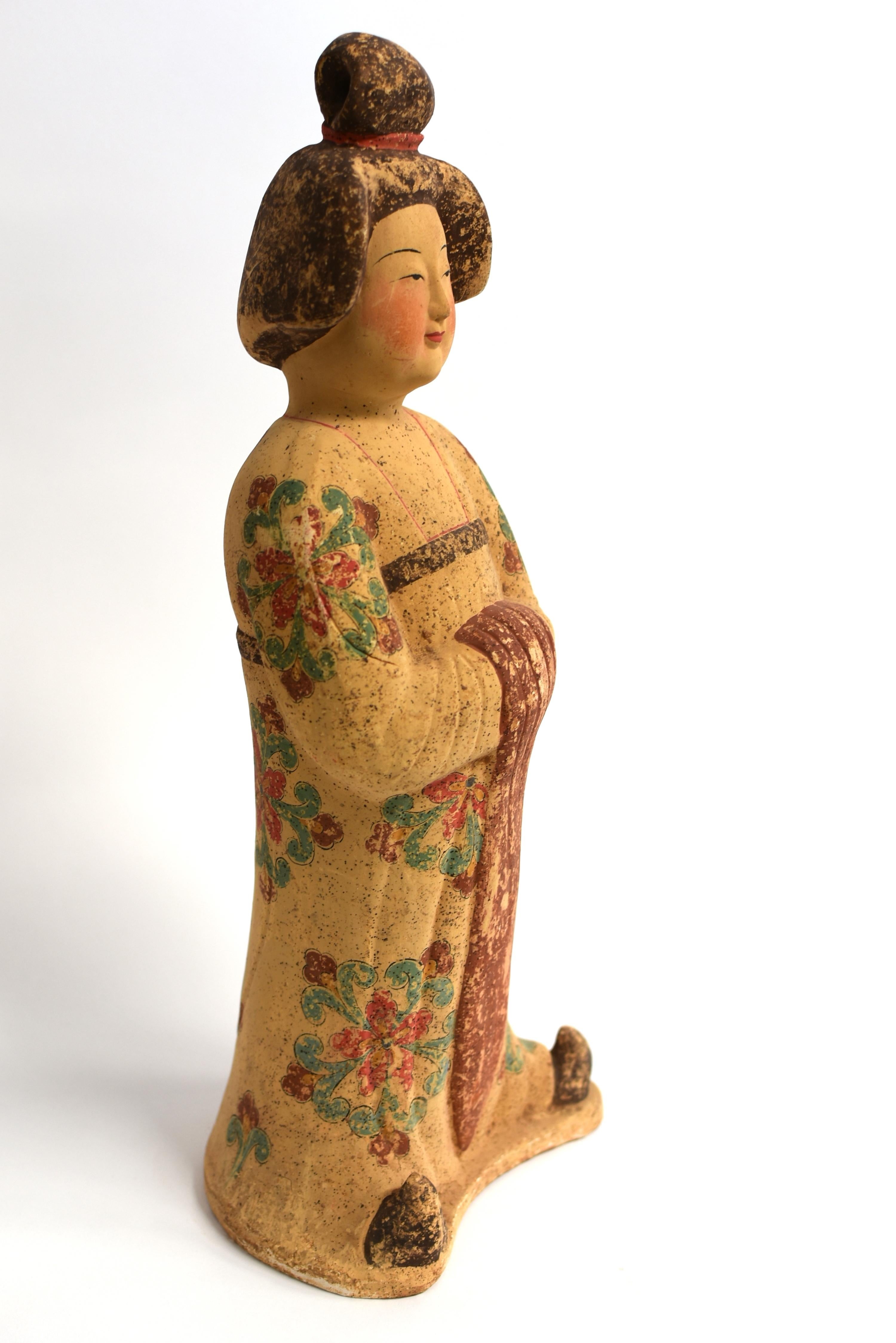 A beautiful hand painted pottery figure of a court lady. The young girl stands with her head tilted slightly to her left. Her face modeled with full, rosy cheeks and delicate features in a small mouth with cherry colored lips and long thin