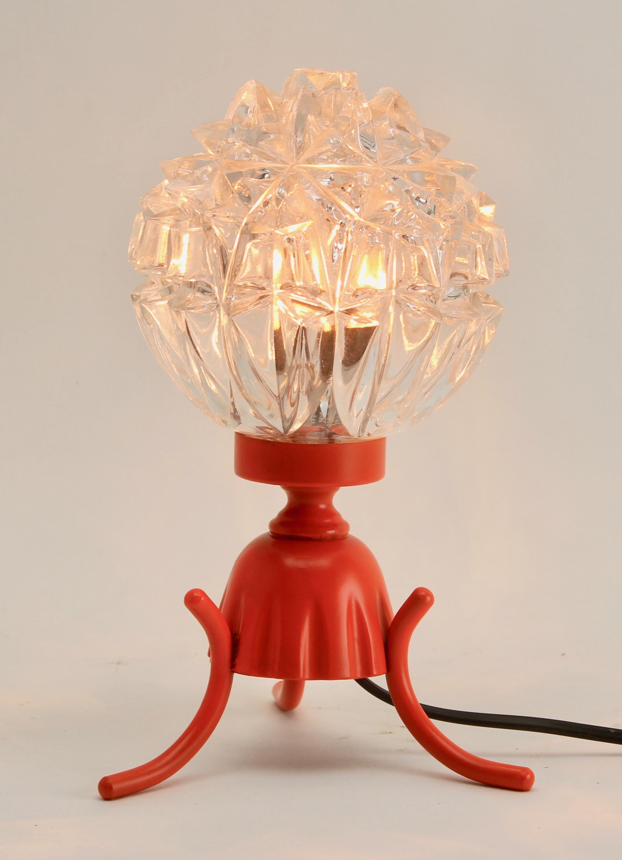 A simple Minimalist base enameled with bright tangerine, to hold a heavy pressed-glass shade that scatters dappled light next to your pillow.
Vintage elements with restored enamel, renovated wiring and fittings.
Electrical lamp fitting E14.

Please