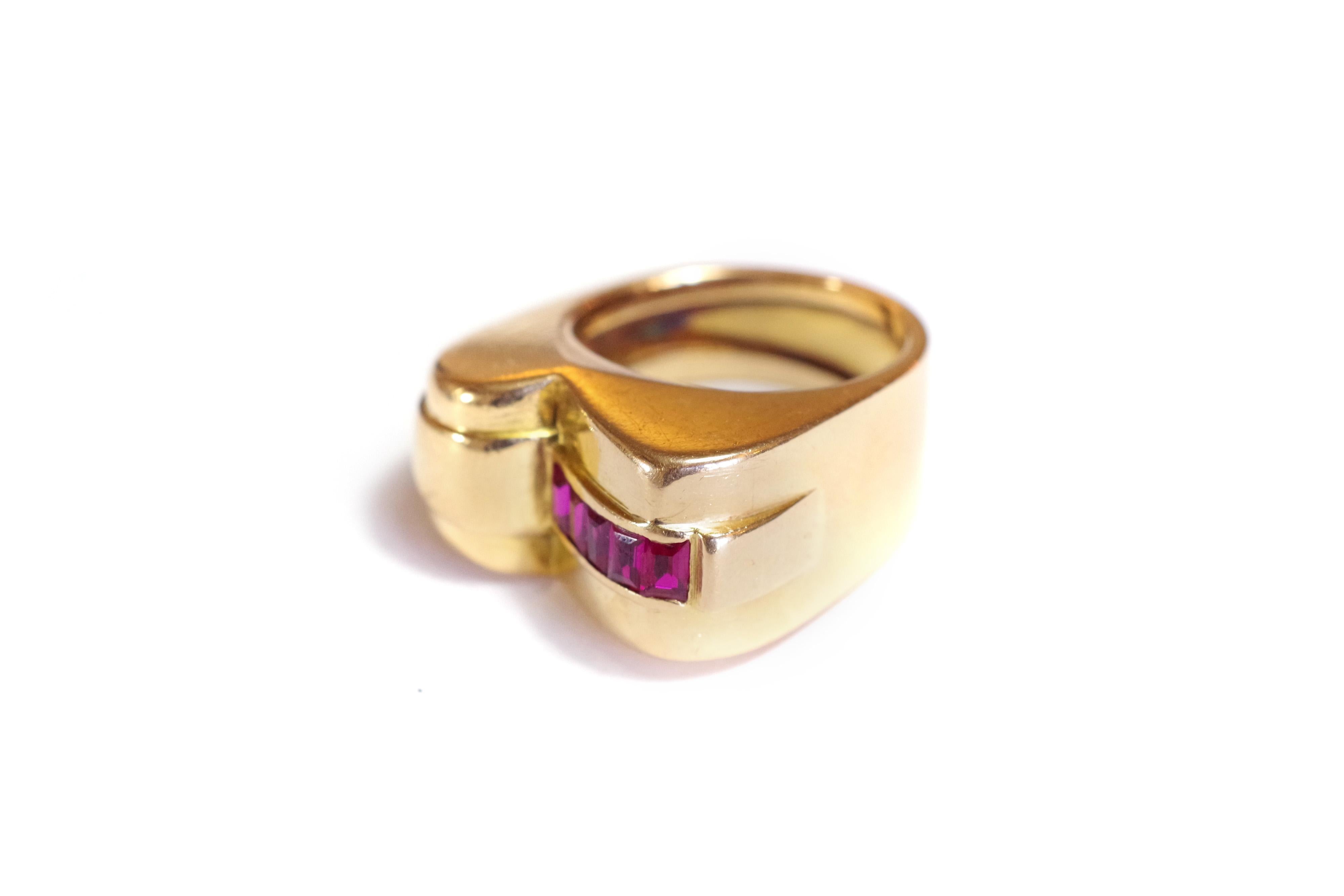 Tank ruby ring in 18k rose gold. The ring is set with a line of five square French Verneuil rubies. The line of rubies is on a flank that meets the center of the ring. A scroll shape opposes the rubies, creating an asymmetry. The shapes and