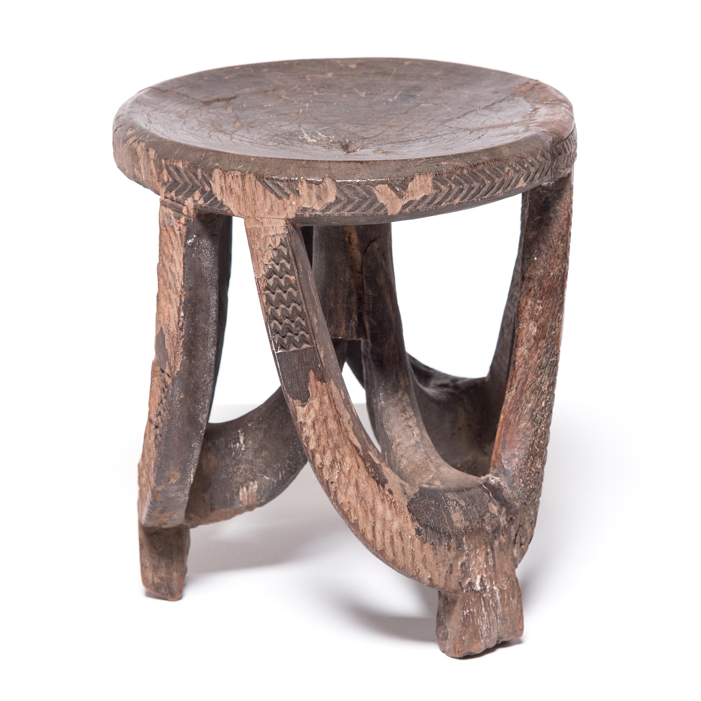 Most likely created by artisans of the Hehe peoples of Tanzania, this tripod stool embodies wonderful movement in its sweeping form. Playful lines drawn by graceful arched legs contrast the stool's clean, round surface. Incised chevron patterns fade