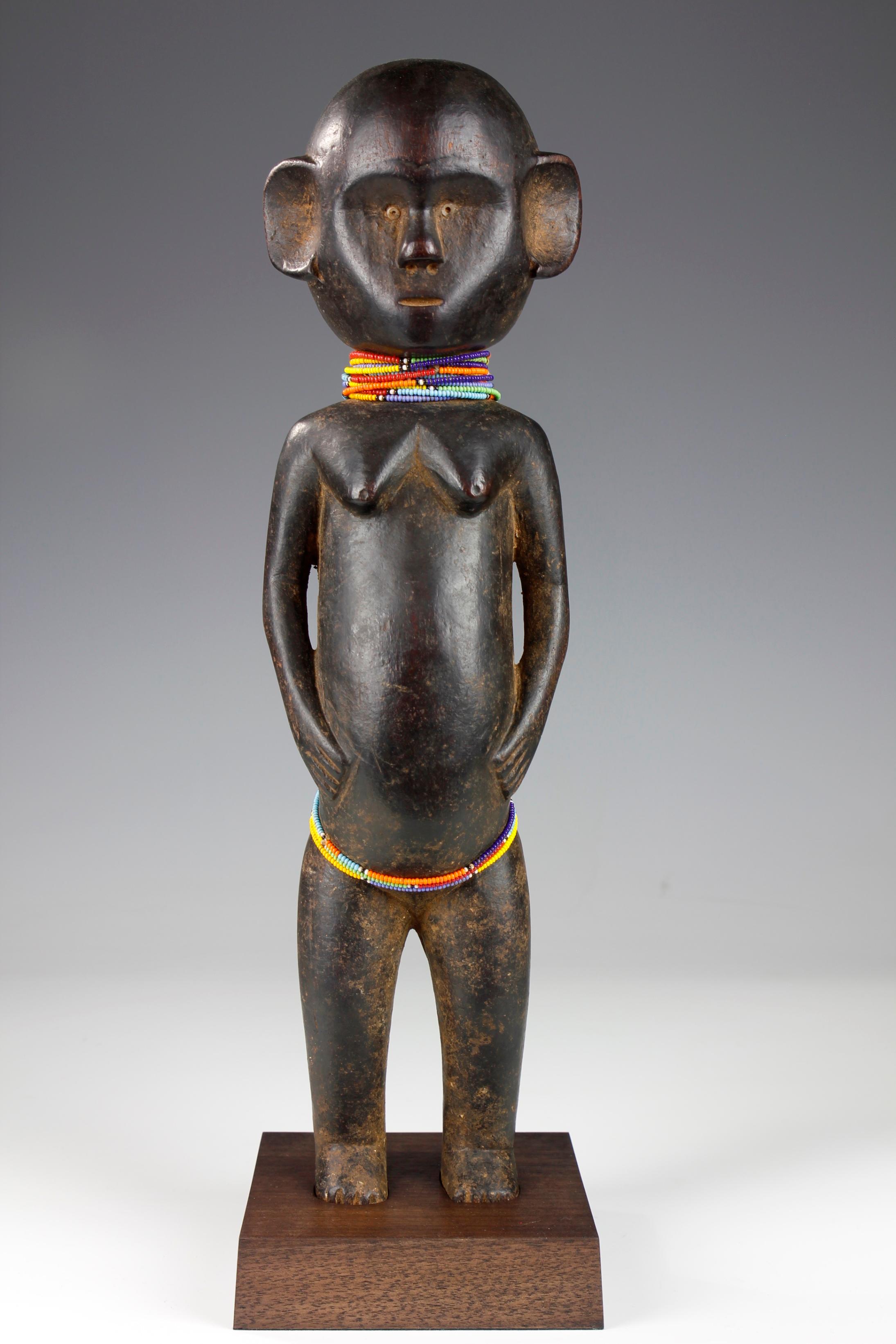 This finely carved mid-twentieth century figurative sculpture, from the Pare culture in Tanzania, depicts a female with large, prominent ears. Standing in a proud, upright stance, she gently rests her hands on her stomach. 

As a type of maternity