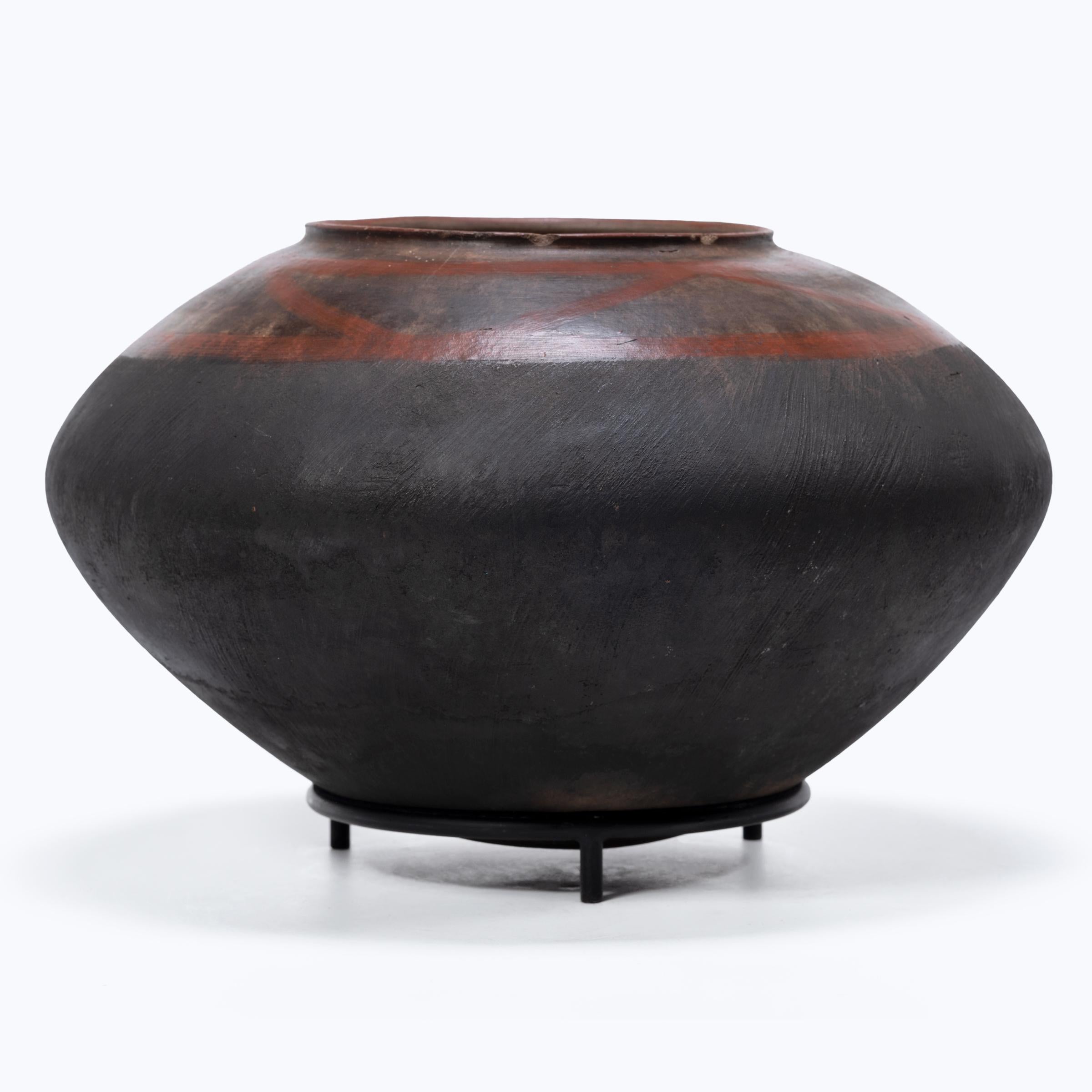 This balanced terracotta pot was used as a storage container by the Nyakyusa people of Tanzania. Bands of red slip pattern the upper portion of the squat vessel, connected by gracefully arched diagonal lines. The lower half is darkened from the