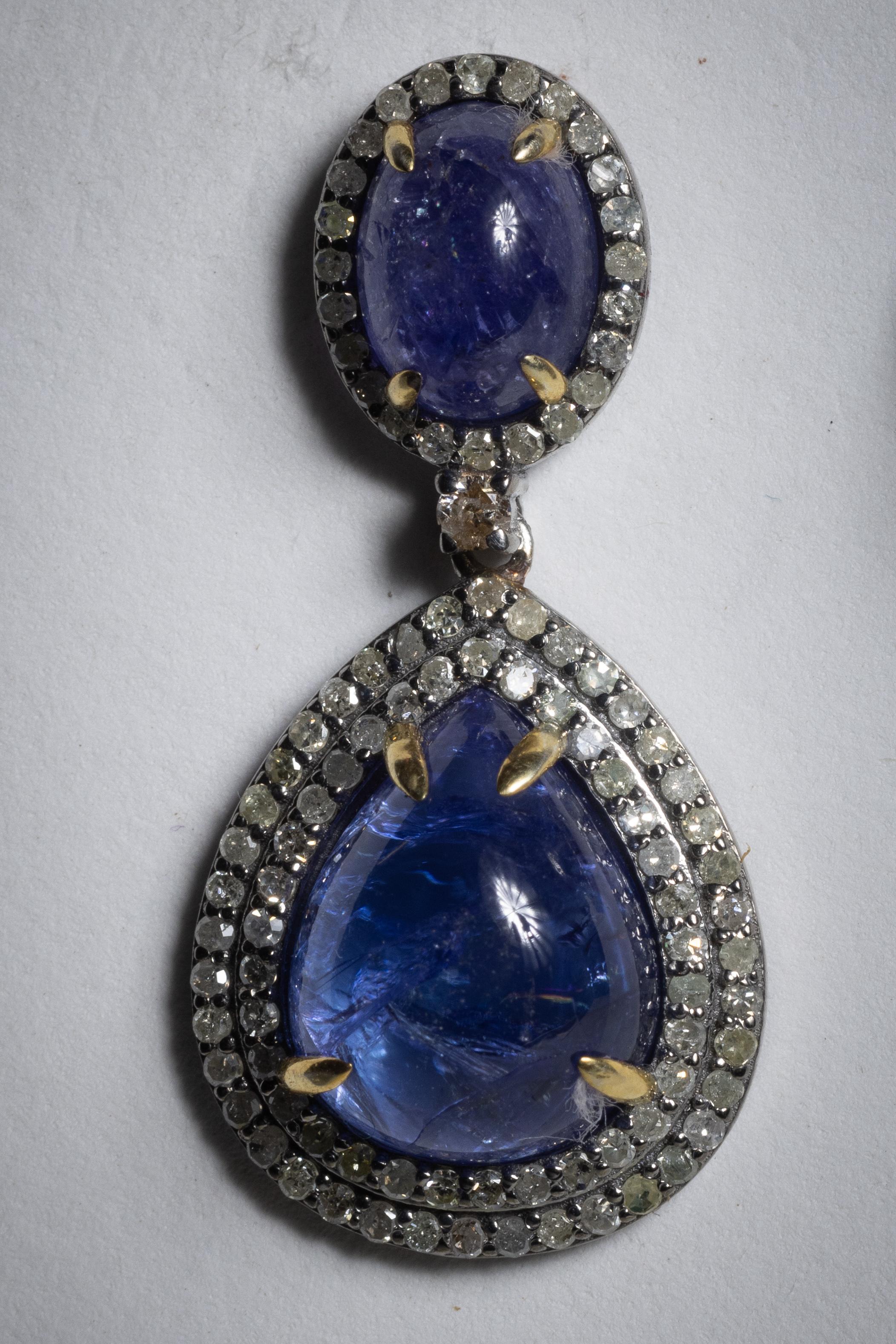 A fabulous pair of drop earrings featuring a large pear-shaped cabochon Tanzanite drop bordered with two rows of round, brilliant cut diamonds.  A an oval cabochon at the post also surrounded with a row of diamonds.  Set in sterling silver with 18K