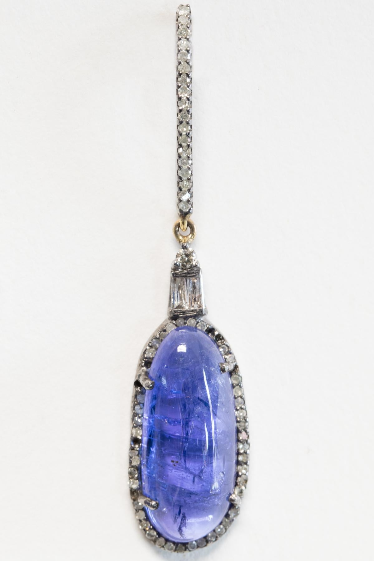 Oval cabochon tanzanite drop earrings bordered in pave`-set diamonds with baguette diamonds above the stone and a single solitaire.  Joins with a linear line of pave`-set diamond post in 18K gold, for pierced ears.  Carat weight of diamonds is 1.26,