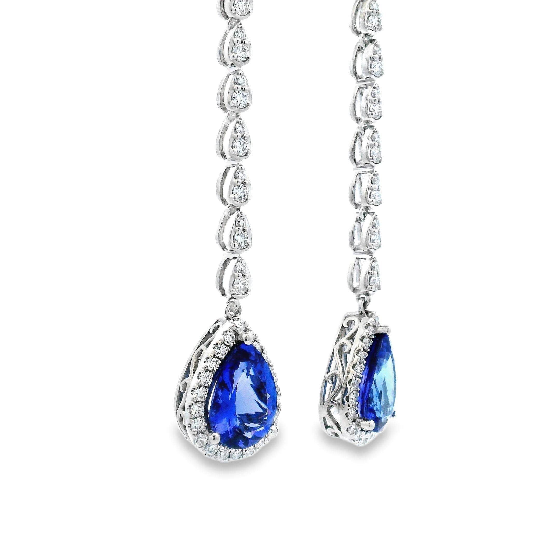 Elegant and eye-catching, these tanzanite and diamond drop earrings are crafted in 14K white gold and designed for movement, sparkle, and impact. Each earring features a vivid pear-shaped tanzanite weighing approximately 2.60 carats, framed in a