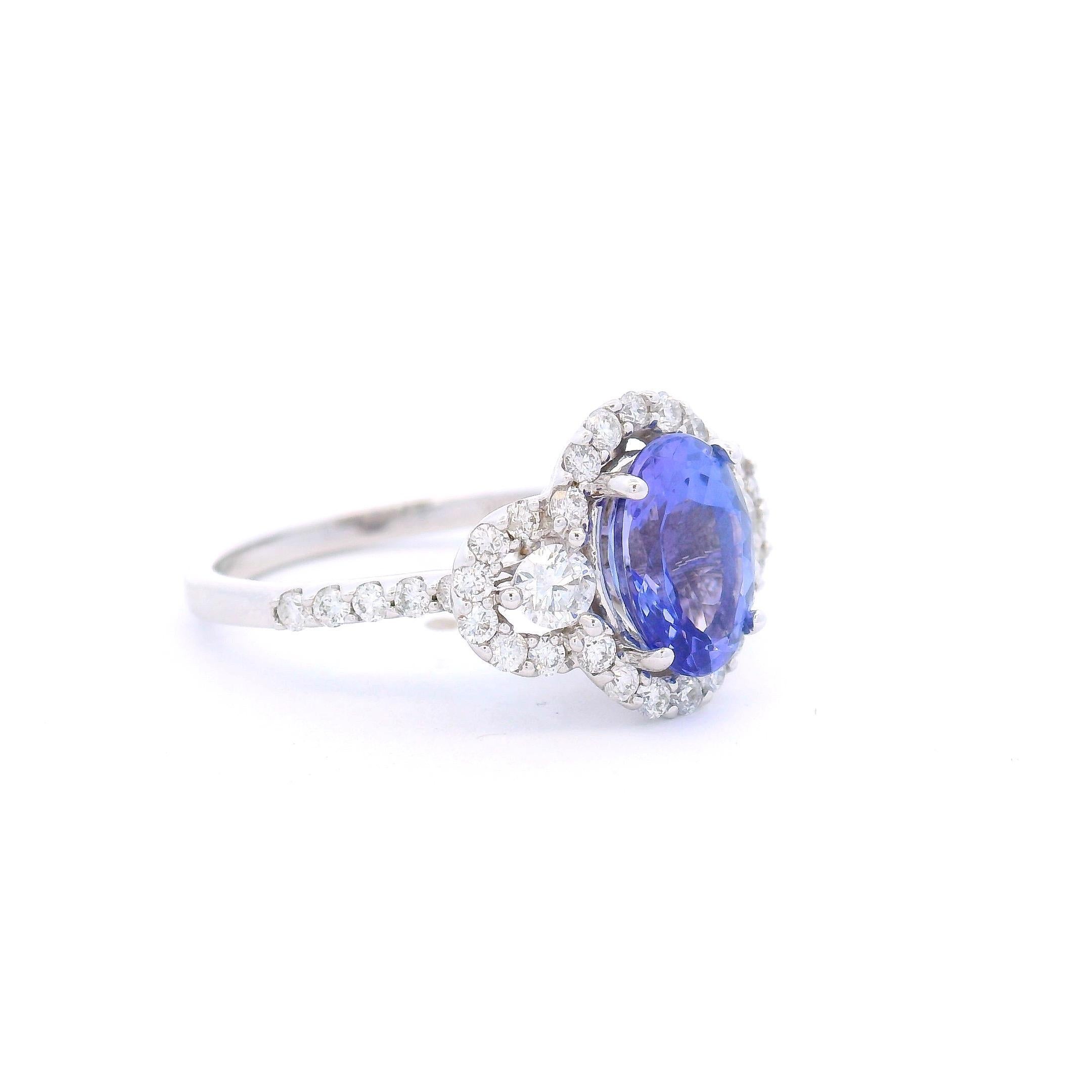 This elegant cocktail ring features a 1.85-carat oval-shaped tanzanite at its center, measuring 9mm x 7mm and held in a classic four-prong setting. The vivid violet-blue stone is framed by a unique triple-halo design: two round diamonds on either