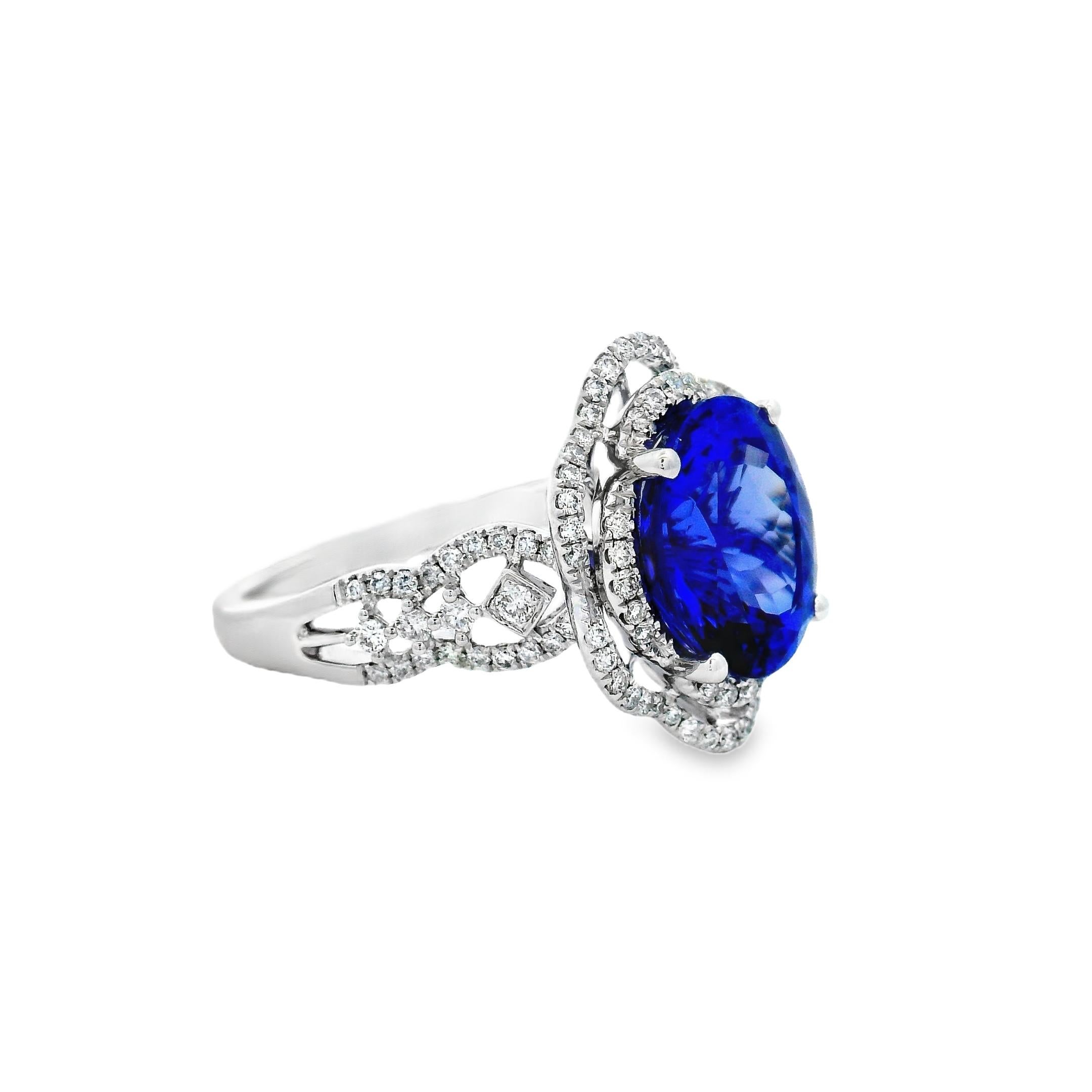 This diamond and tanzanite ring centers on a vivid 4.3-carat oval-shaped tanzanite, measuring 11mm x 9mm, set in polished 14K white gold. The richly saturated violet-blue stone is held by four prongs and framed by a layered diamond halo with