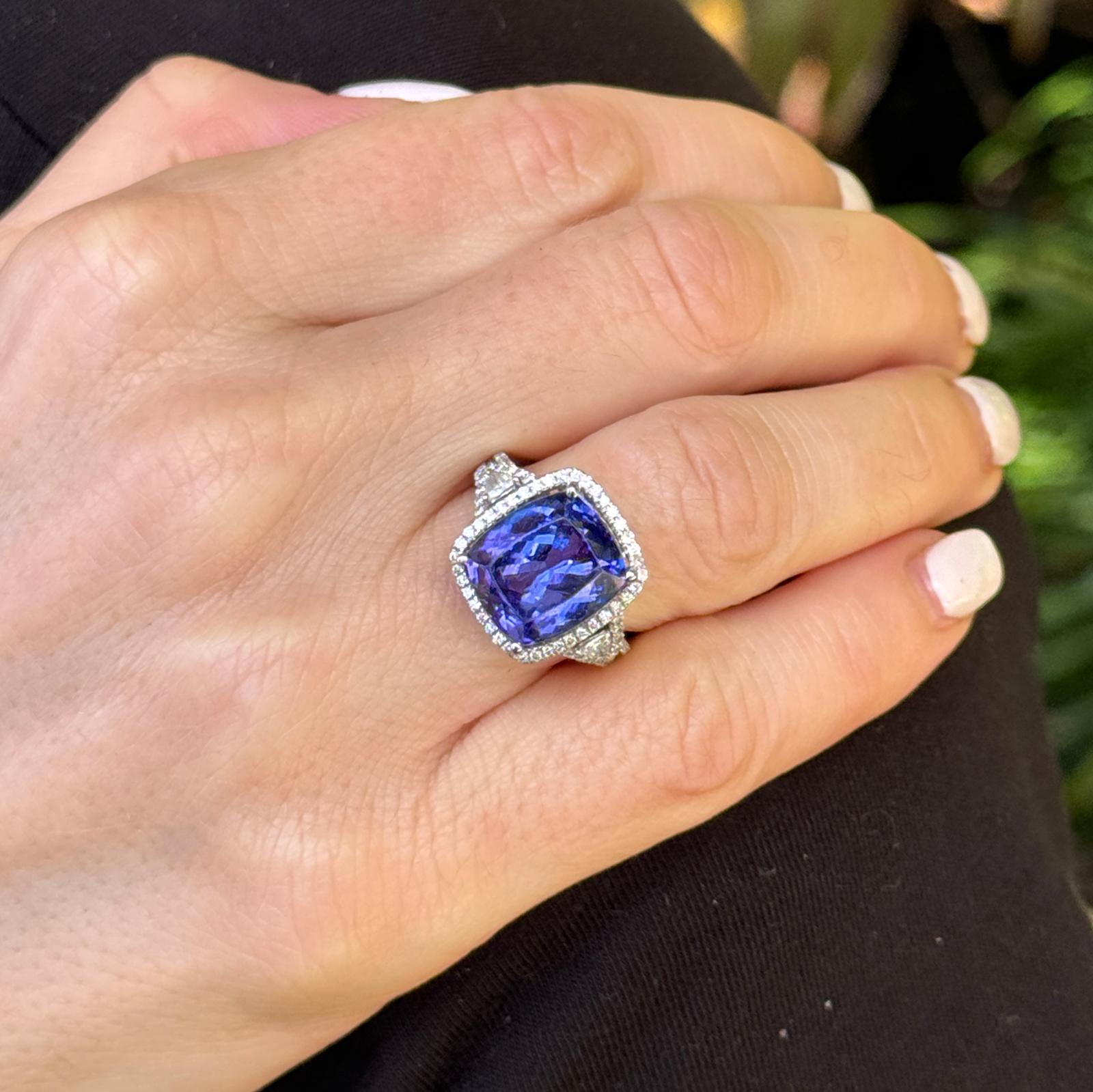 This breathtaking ring features an approximately 8-carat oval tanzanite as its centerpiece, showcasing a vivid, deep blue-violet hue that is both rare and captivating. Flanking the tanzanite are two trillion-cut diamonds, adding symmetry and