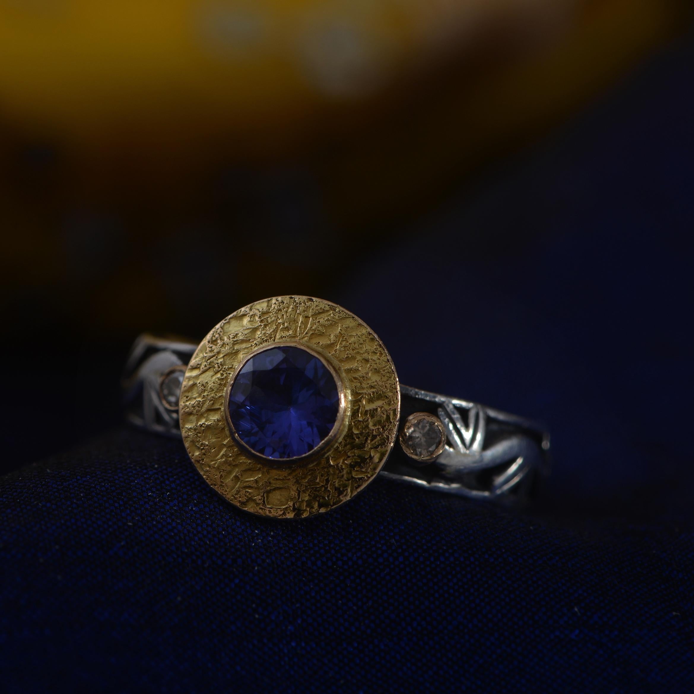 This lovely tanzanite ring is one-of-a-kind. Handmade in our workshops, it features a central tanzanite which is set in 18k gold, and flanked by two full cut diamonds, which are also set in 18k gold. The shank is made of oxidized sterling silver,