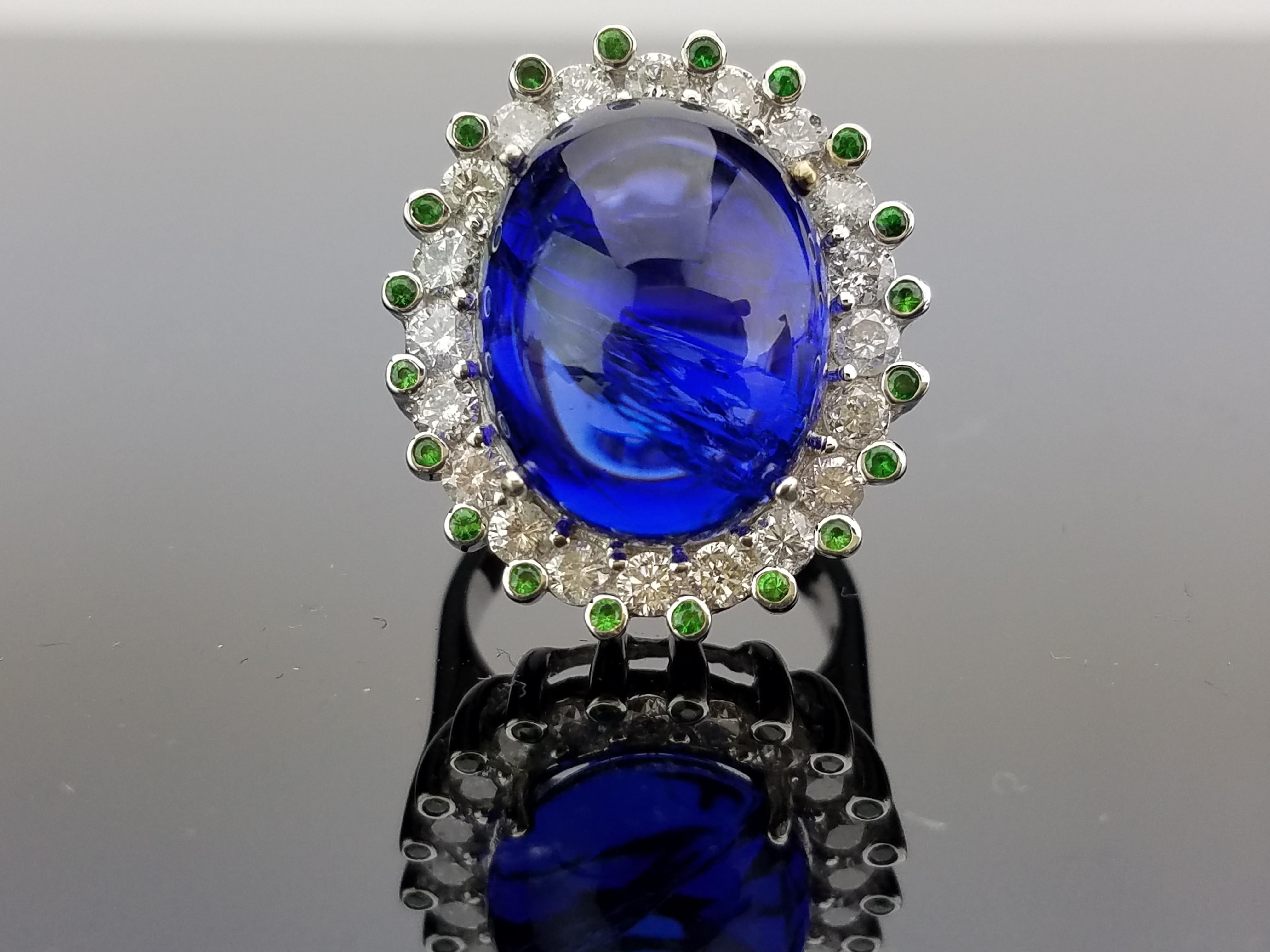 Statement-Cocktailring aus Tansanit, umgeben von einer einzelnen Diamantstufe und einem grünen Granat, montiert auf einem Band aus 18 Karat Weißgold. 

Details zum Stein: 
Stein: Tansanit, ovaler Cabochon, 19,78 Karat
Stein: Tsavorit, rund, 0,26