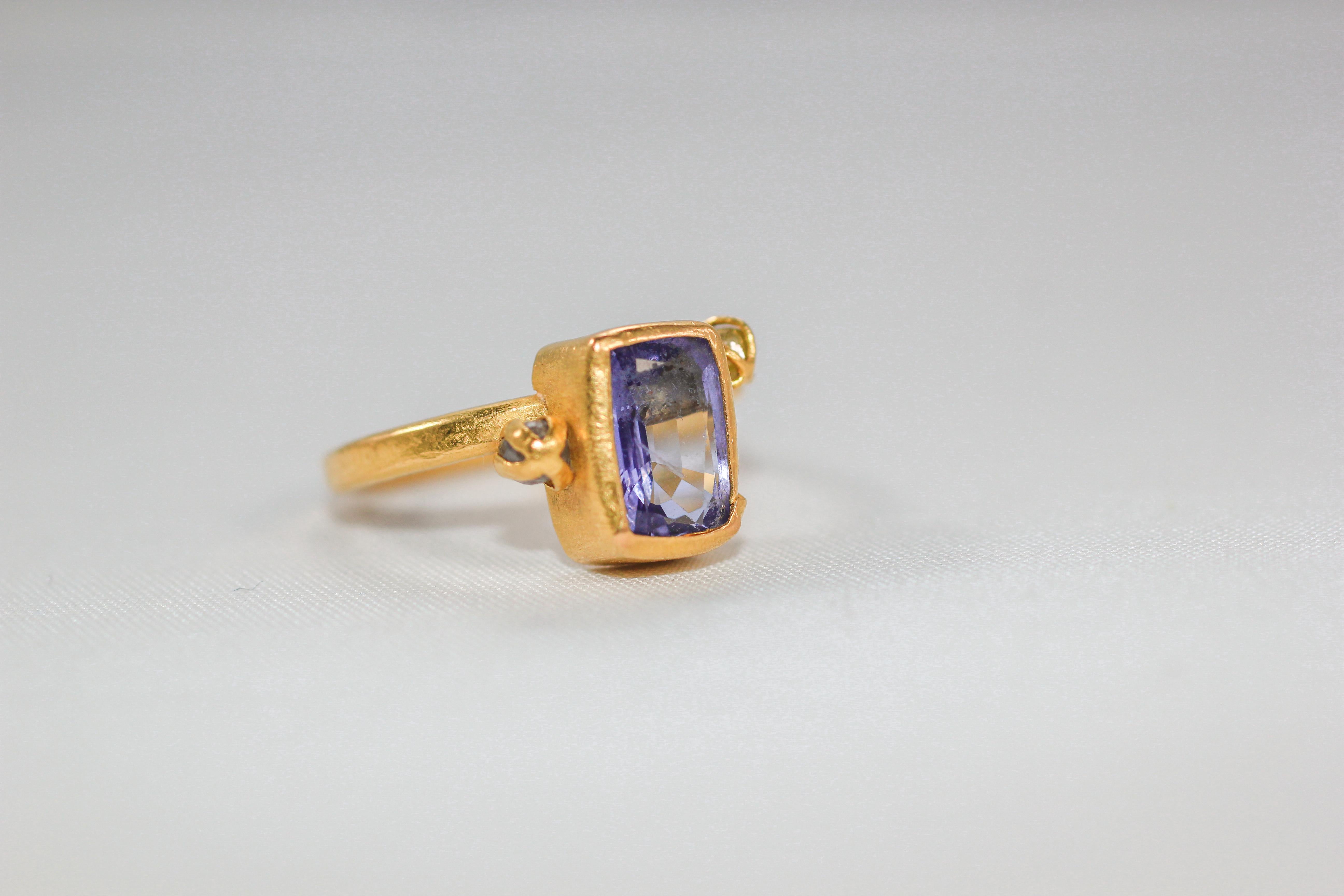 Pastel purple emerald cut Tanzanite is set in 22k solid gold bezel atop of a 21K gold shank. This three-stone fashion ring design is asymmetrical and features an unusual textured bezel and crisscross settings for the diamond briolettes. Popcorn ring