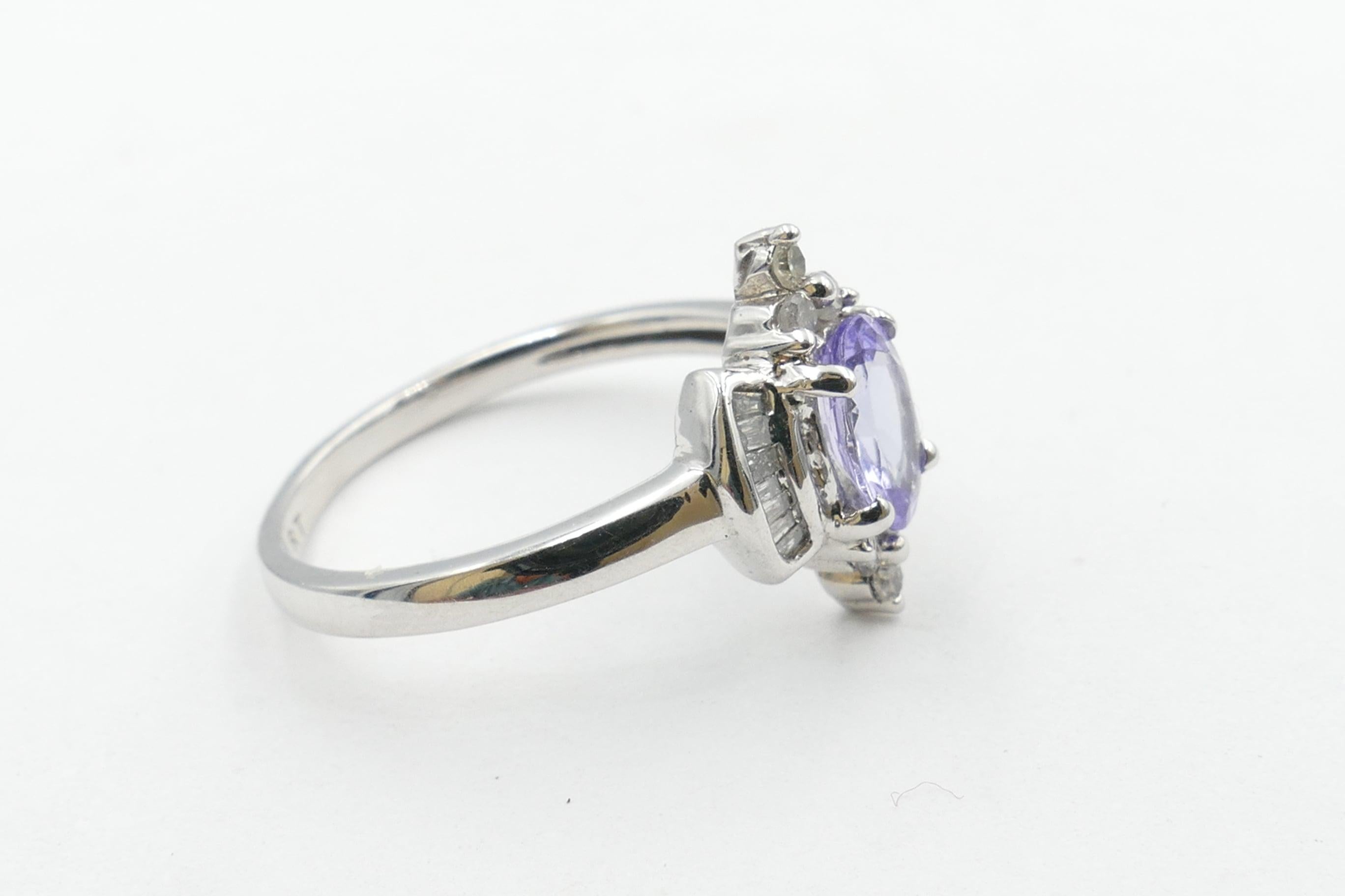 What a very different look this beautifully shaped Tanzanite creates. Oval Cut, around 1 carat, of purplish-blue Colour, Medium Tone, eye-clean Clarity & 4 claw set.
It is flanked by 6 Round Brilliant Cut Diamonds, with a further 14 tapered Baguette