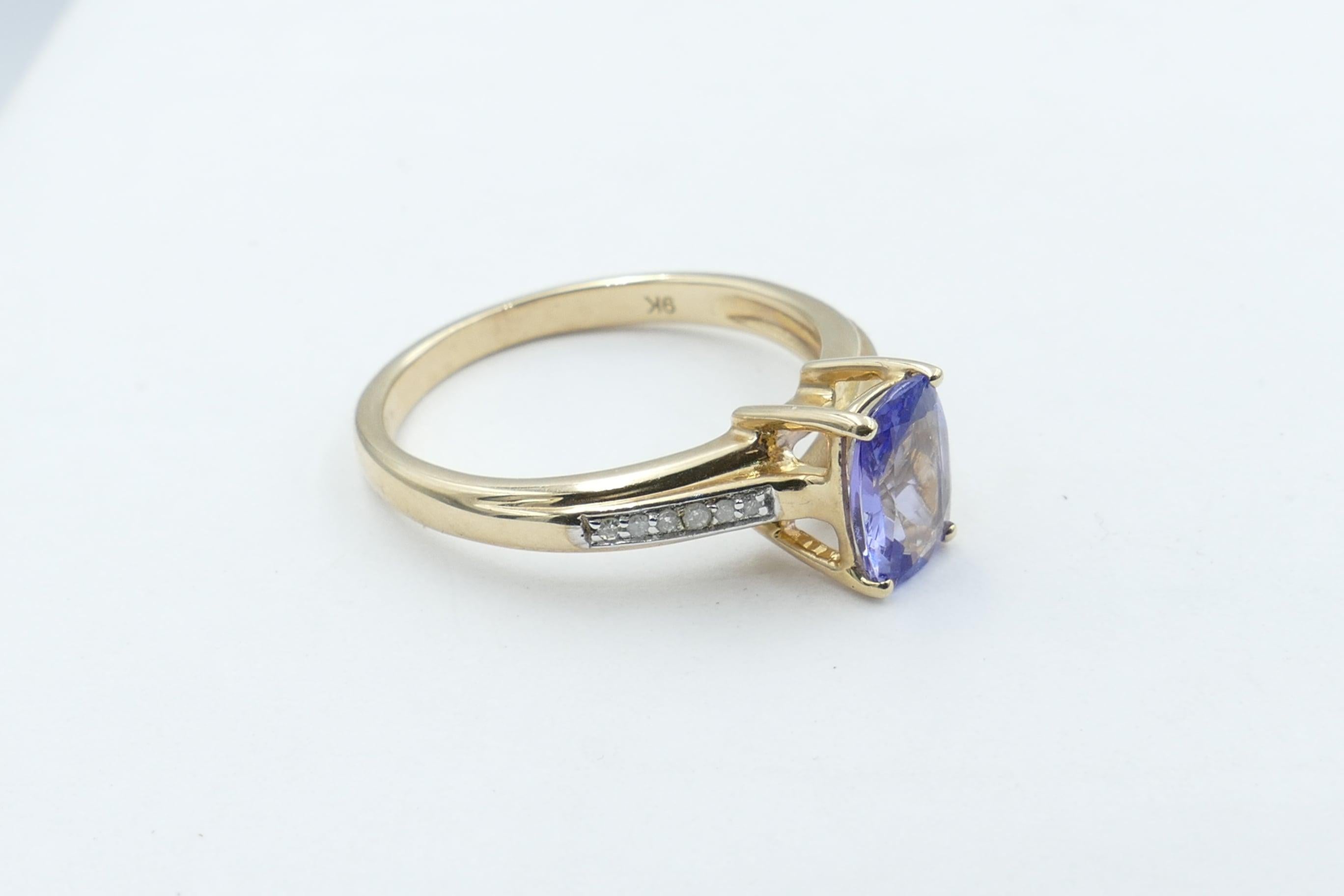One 1.34 carat Tanzanite with Colour of Purplish-blue, Tone medium, Clarity eye-clean, Rectangular Cushion Cut, 4 claw set, is flanked by 12 Single Round Cut Diamonds J/K Colour Clarity I1-I2 makes up this very versatile Ring that presents as an
