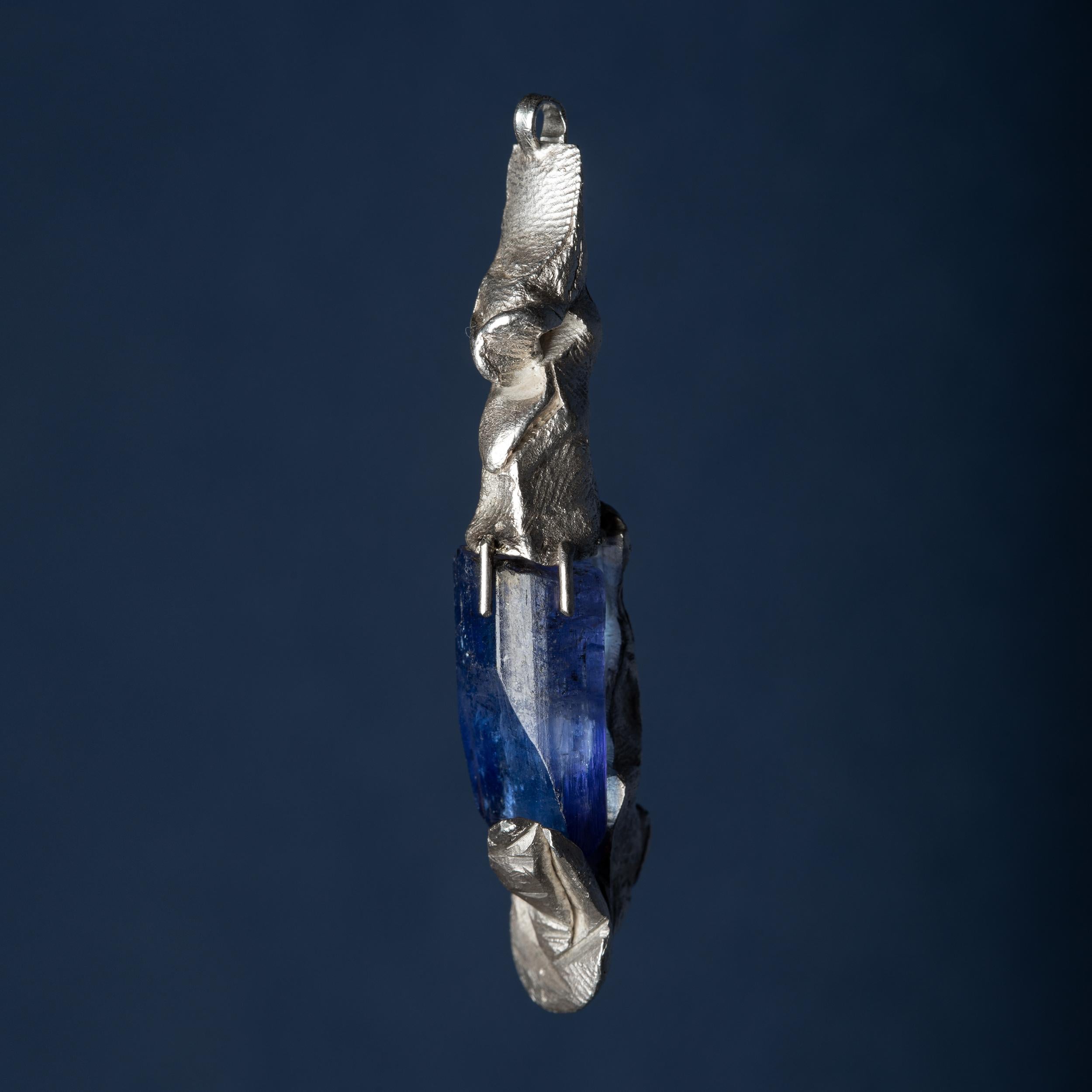 The Observer sits on top of his throne: a stunning rough tanzanite crystal that is beautifully terminated and shows vivid blue and purple. The front figure references ancient Egyptian statues. The crystal itself rests on the back of another face