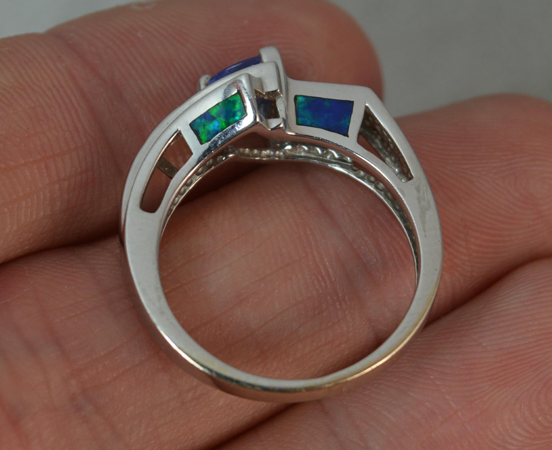 A superb ladies Tanzanite, Opal doublet and Diamond ring.
Solid 14 carat white gold shank and setting.
​Designed with a natural trillion cut tanzanite to centre, 5.7mm. To the side a dark green blue opal doublet panel, the other side three small