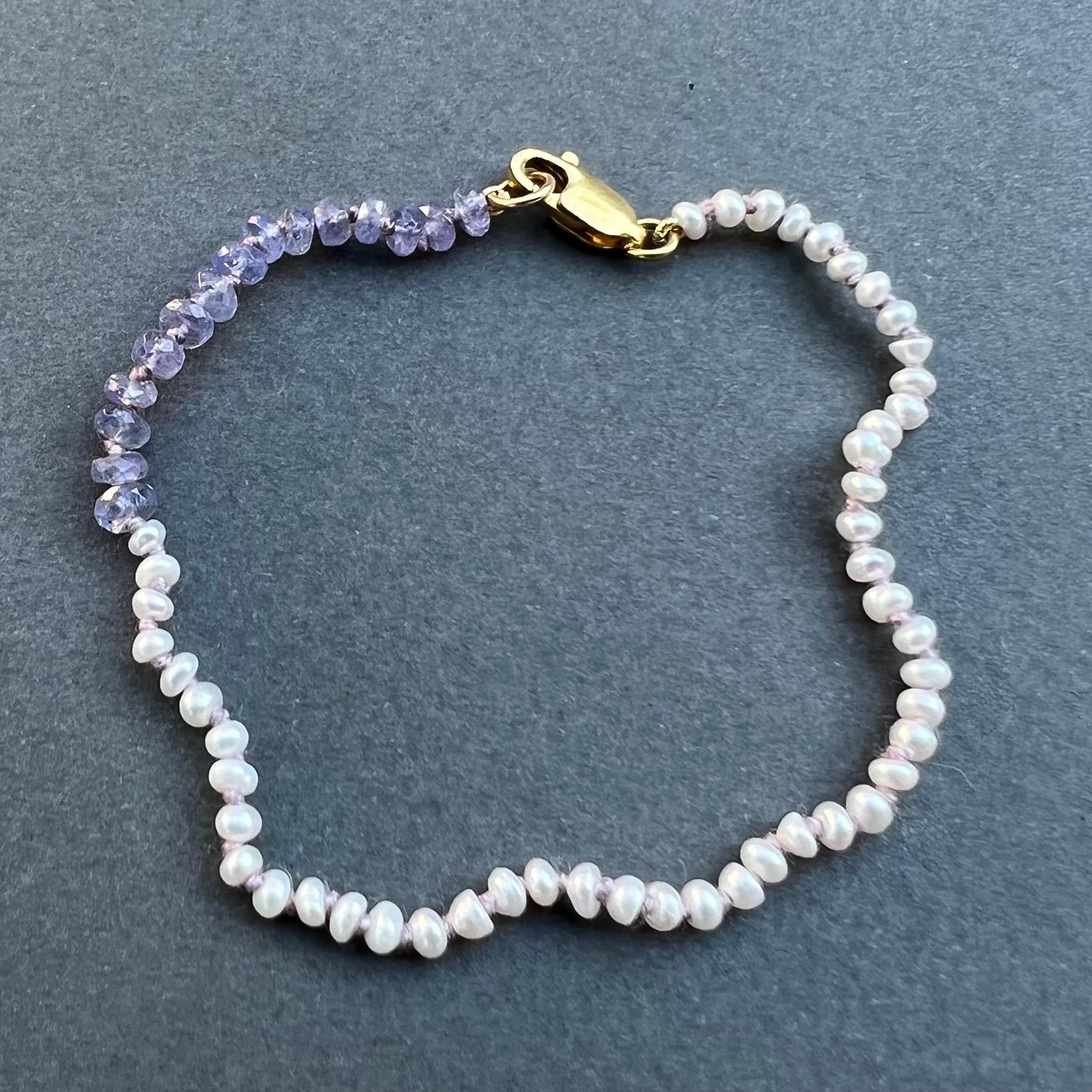 White Pearl Tanzanite Beaded Bracelet 
Lilac Silk Thread 
Designer: J Dauphin
Metal: Gold Filled Clasp

J Dauphin jewelry is hand made in Los Angeles and was created by designer Johanna Dauphin. Most of the jewelry is unique or created in small
