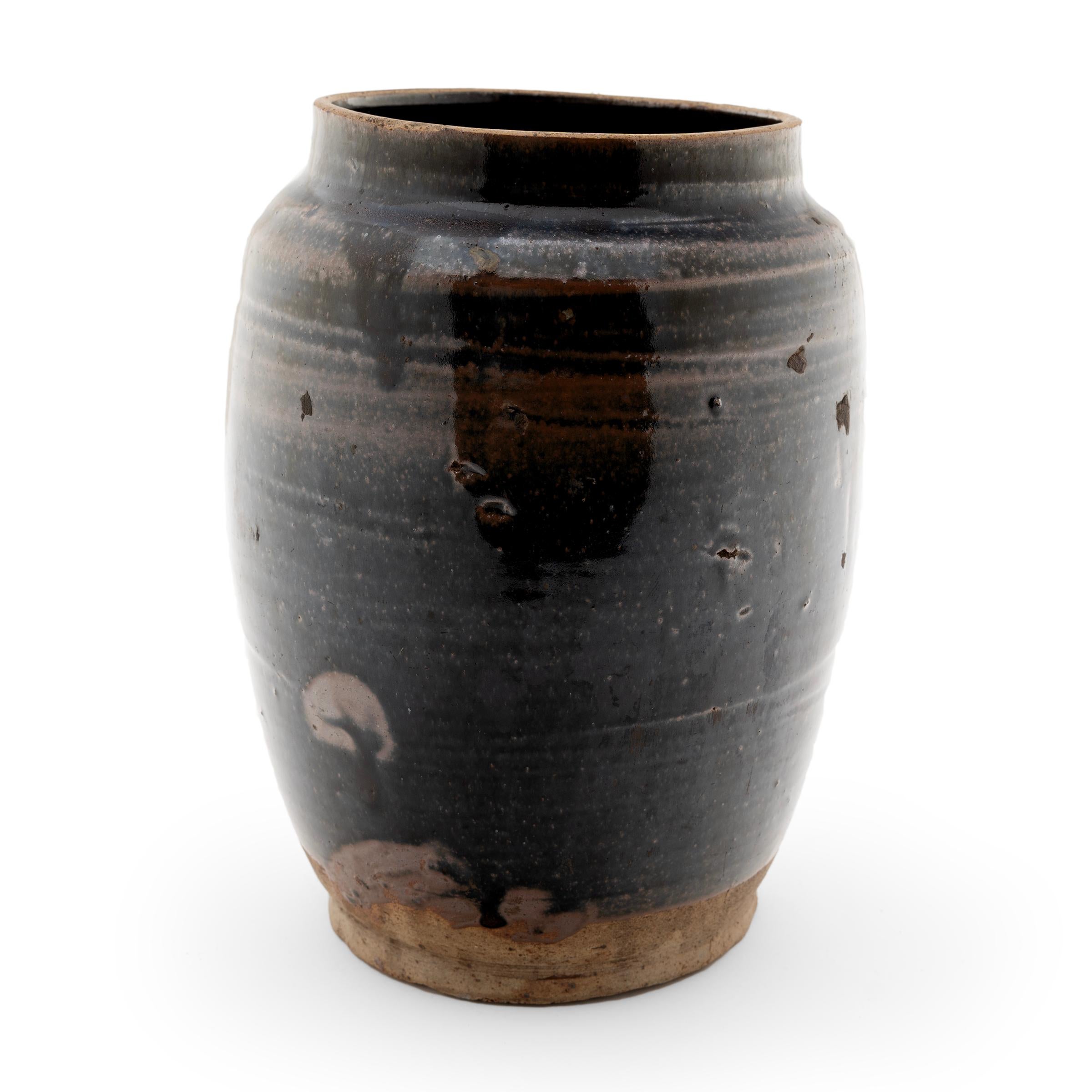 Originally used to store foods or pickle vegetables in a provincial Chinese kitchen, this late 19th-century ceramic jar is coated inside and out with a richly-colored dark glaze. The thin glaze drips down the sides, allowing the ripples of its spun