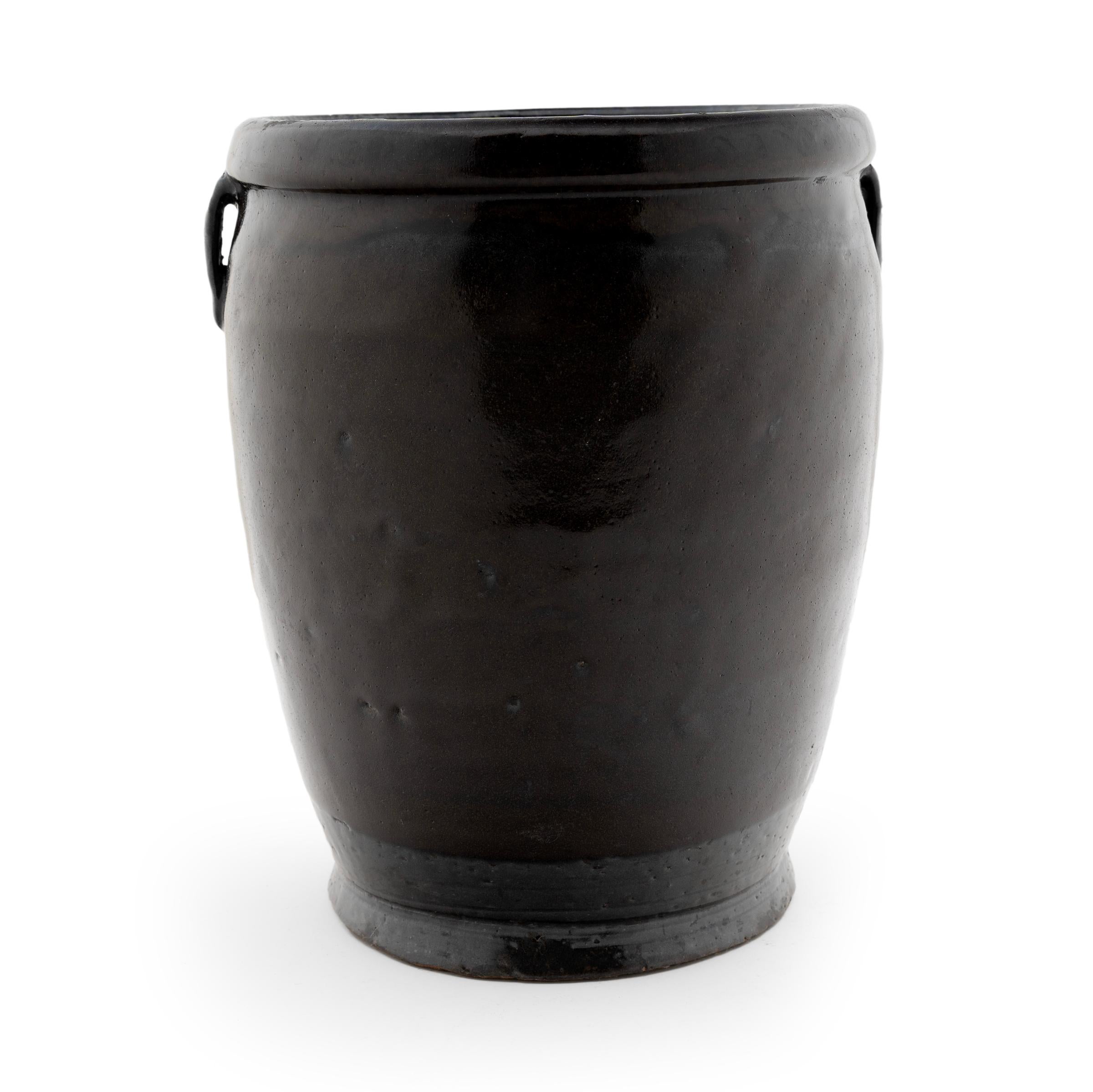 A rich, dark brown glaze coats the gently tapered form of this late 19th-century kitchen jar. As evidenced by the glazed interior, the jar was once used daily in a Qing-dynasty kitchen for fermenting foods and condiments. The wide-mouth jar stands