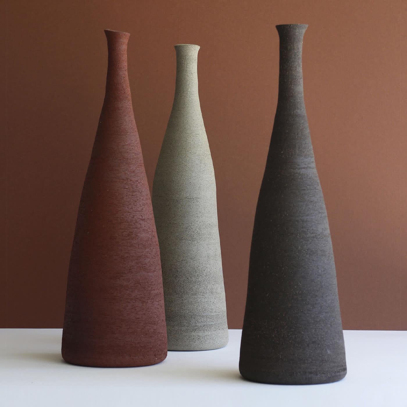 A sophisticated sculptural silhouette defines this singular stoneware vase, an exclusive and warm addition to contemporary settings. Deftly crafted by hand and naturally unique, it flaunts a deep reddish tone enhanced by a scratched texture for a