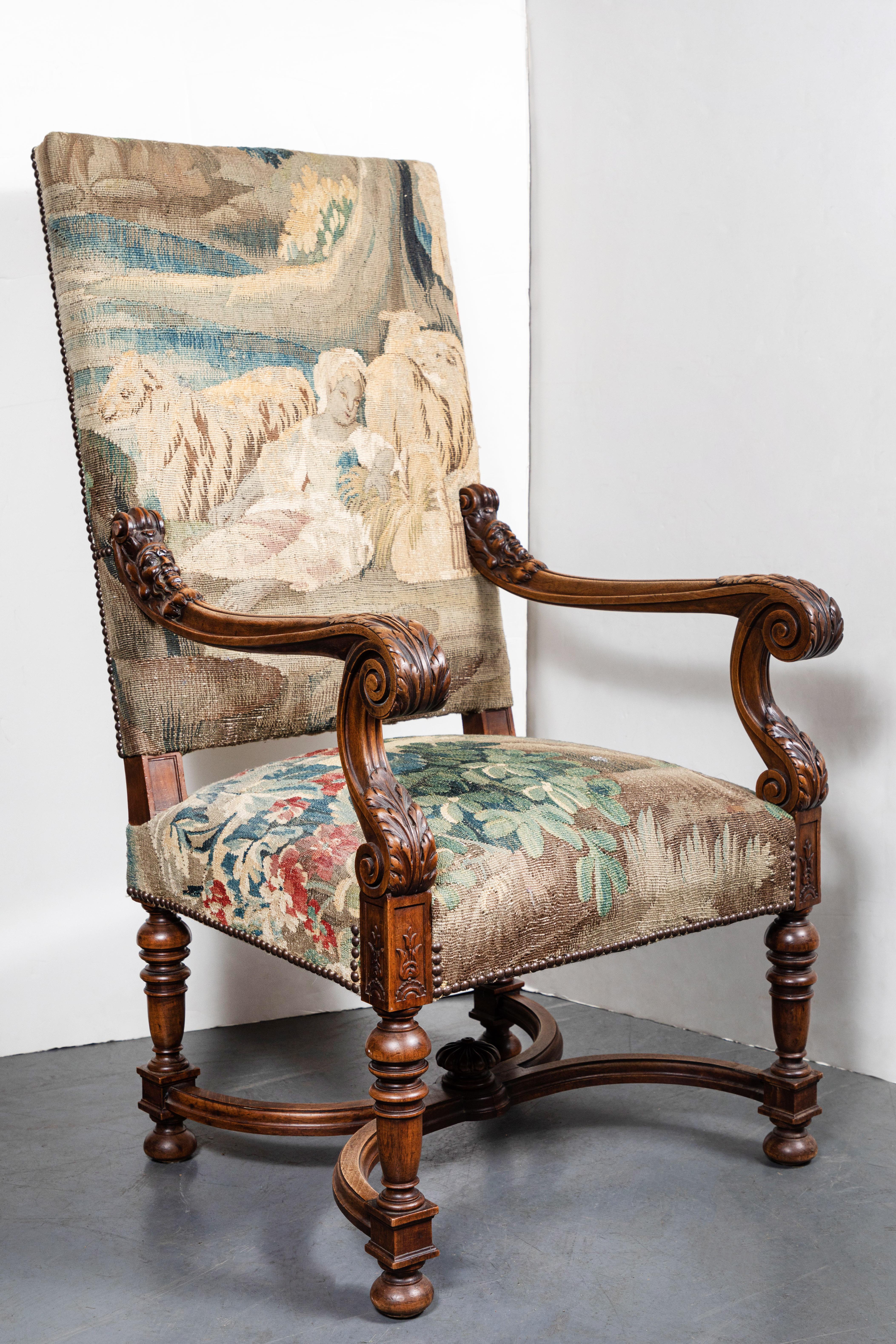 Elegant fauteuil français sculpté, vers 1850, dont les accoudoirs sont ornés de volutes et de feuillages, et dont le brancard est en forme de X. L'ensemble est recouvert d'une tapisserie flamande du XVIIIe siècle, ornée de têtes de clous en bronze.