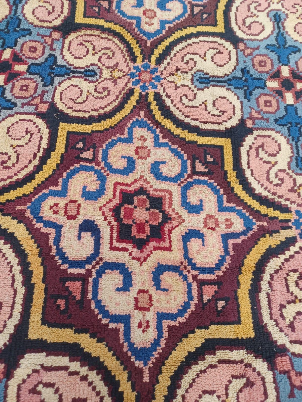 Alfombra anudada a mano  en Francia, en la ciudad de Cogolin, con un fondo de color marrón y un diseño continuo estilizado en tonos rosas y azules. Estas alfombras se hacían en piezas pequeñas y luego se unían.  Tiene dos restauraciones menores