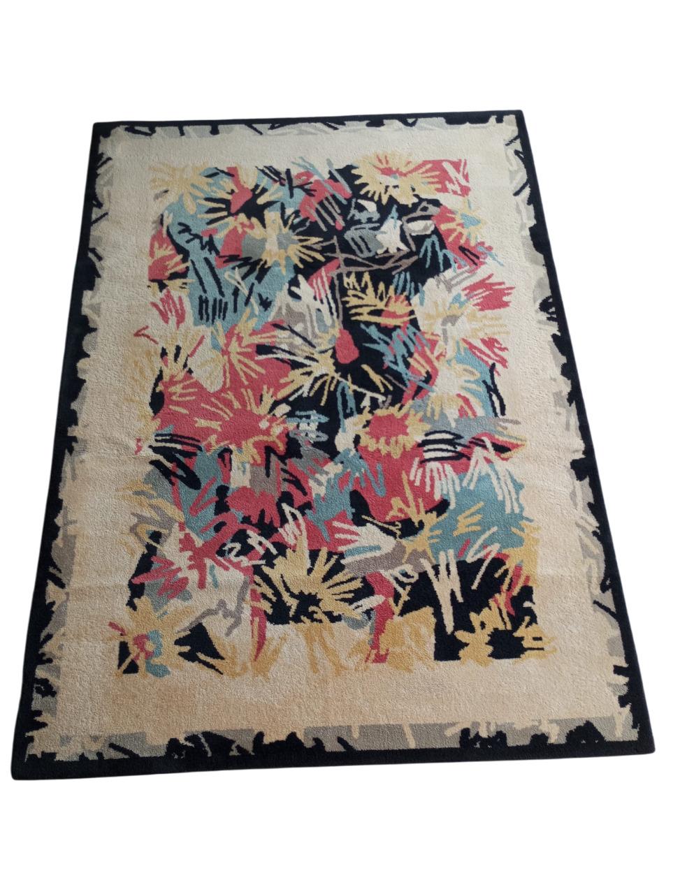 Size 235 cm. x 170 cm.
This abstract and vibrant rug design has a beige and black frame enclosing a richly colored central pattern.
The central part features irregular shapes with shades of yellow, red, blue, black and beige. The shapes overlap and