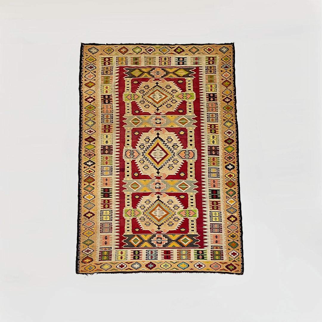 Teppich im ethnischen oder kaukasischen Stil, mit mehrfarbigem Kurzflorgewebe und Fransen am ganzen Umfang.
Vielfältiges geometrisches Muster, das sich über die gesamte Oberfläche des Teppichs erstreckt.
1970 ca.
Guter Zustand, Gebrauchsspuren auf