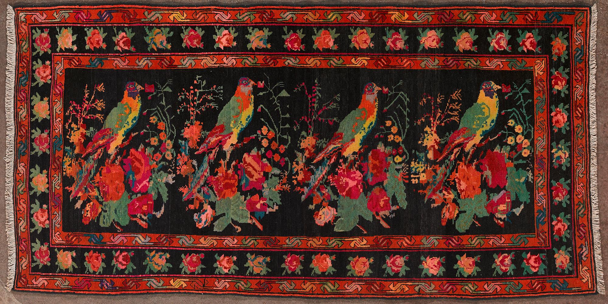 The carpet with a lively, painterly aesthetic. The surface features floral and naturalistic motifs with large colorful birds in the center and a richly decorated border. The basic color is black, with vibrant shades of red, green, orange and yellow.