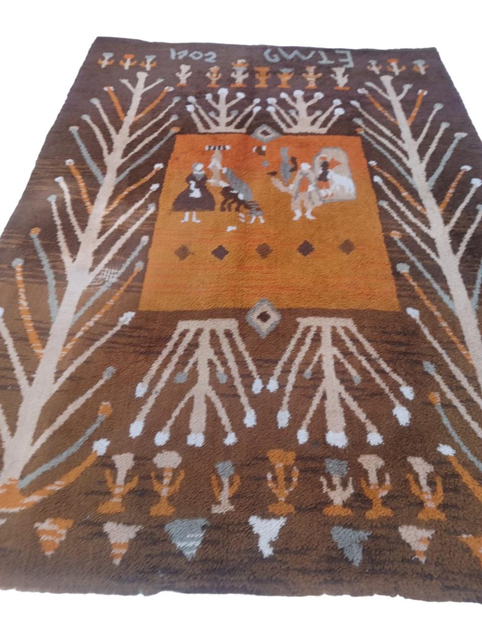 Teppich aus den 1960er Jahren, Maße 280 x 198, aus Wolle.  Der orangefarbene Hintergrund mit brauner Umrandung hebt ein stilisiertes Design mit Pflanzen und Schriftzeichen auf orangefarbenem Hintergrund hervor, das eine rustikale und doch