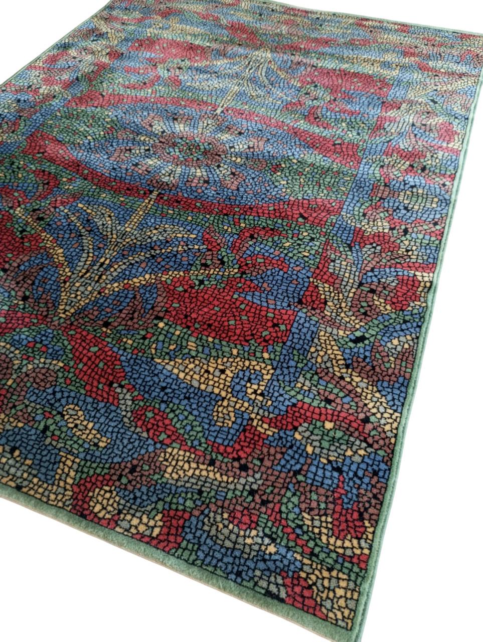 Tapis français en laine à motif mosaïque, dans le style d'Henry Christine.
Le motif rappelle une mosaïque byzantine ou romaine, avec de petites tesselles stylisées créant l'effet visuel de pierres colorées. Les motifs sont symétriques et floraux,