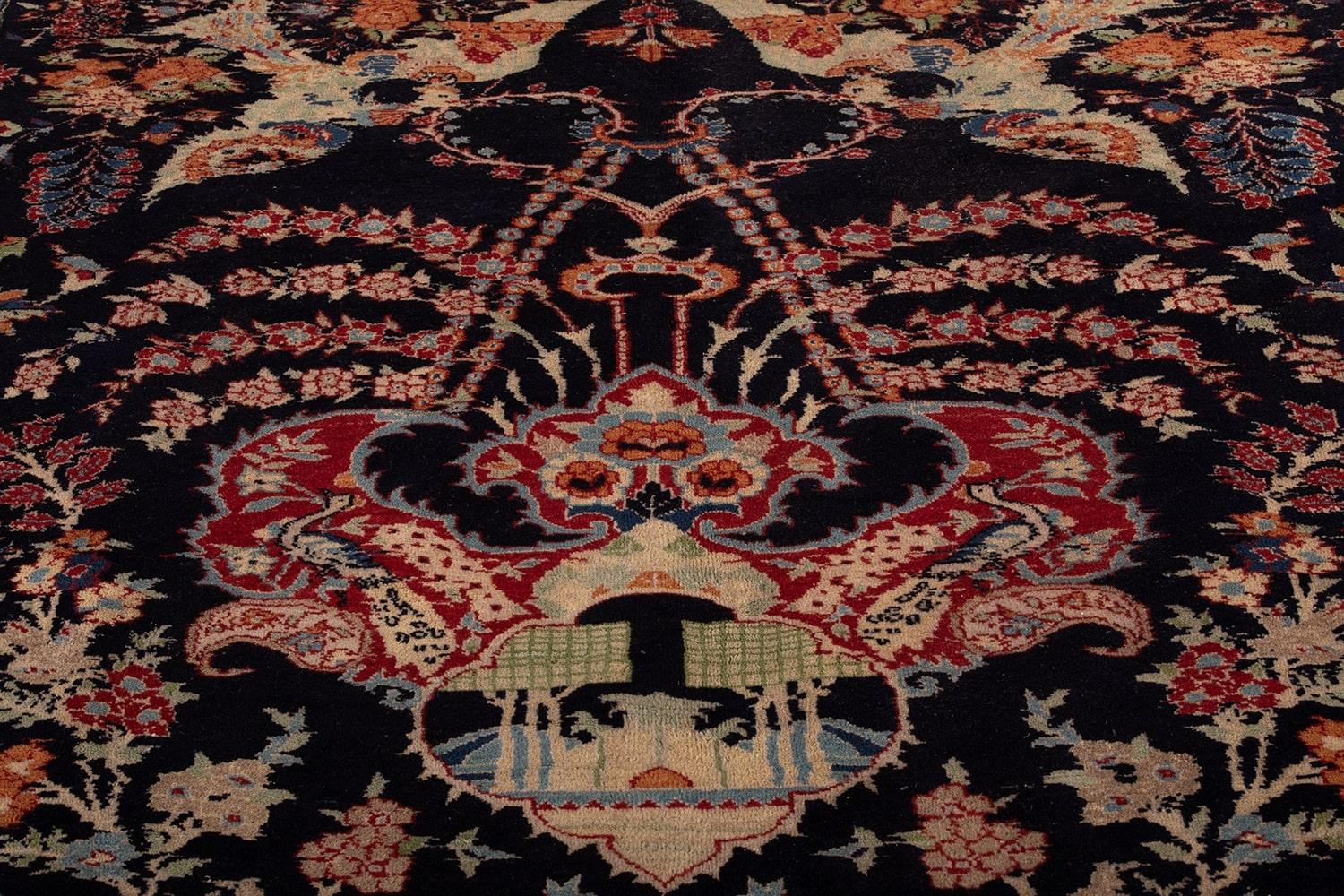 Tappeto Agra, annodato a mano, caratterizzato da un medaglione centrale, incorniciato da motivi floreali e naturali su sfondo scuro e una bordura rossa con motivi ornamentali minuti. Realizzato in lana, i colori caldi e freddi si uniscono per