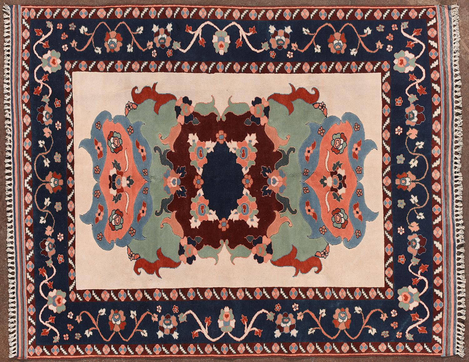 Alfombra anudada a mano procedente de Kazajstán, fabricada entre los siglos XX y XXI. Presenta un motivo central espejado y simétrico con formas florales y abstractas en tonos rojos, azules, verdes y beige. La cenefa, decorada con flores estilizadas