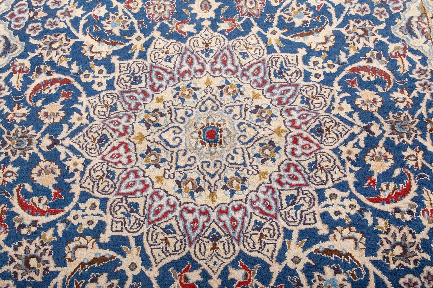 Tappeto Nain in stile persiano tradizionale, annodato a mano, caratterizzato da un medaglione centrale raffinato con motivi floreali stilizzati e una fitta decorazione di rami e palmette su campo beige chiaro, incorniciato da una bordura blu con
