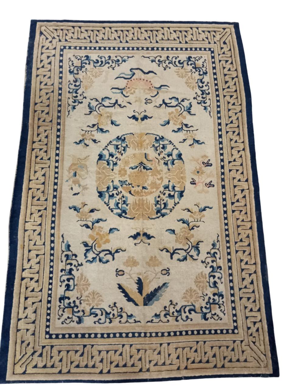 Tappeto cinese metà XIX sec., annodato a mano in lana, colore del fondo beige con bordura finale in blu, colore che caratterizza i tappeti cinesi.
Ha un medaglione centrale ornato da peonie, e altri fiori simbolici. La sua bordura è molto