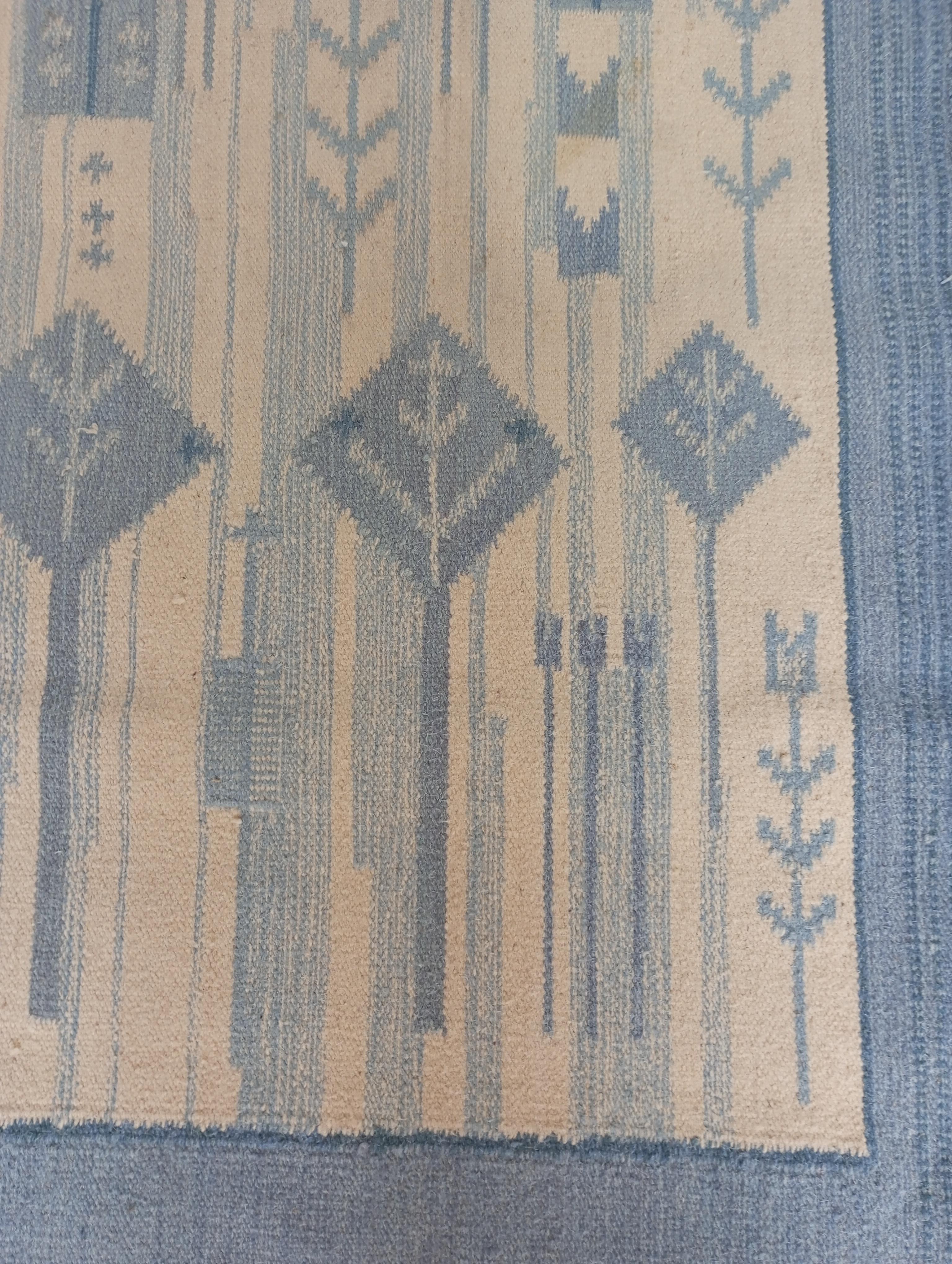 Swedish 1960s rug-arazzo attributed to Eva Nemeth with a stylized design, measuring 238 cm. x 172 cm. The white background enhances the light blue design, which depicts a group of horses with flowing tails. One of them led by a female figure.