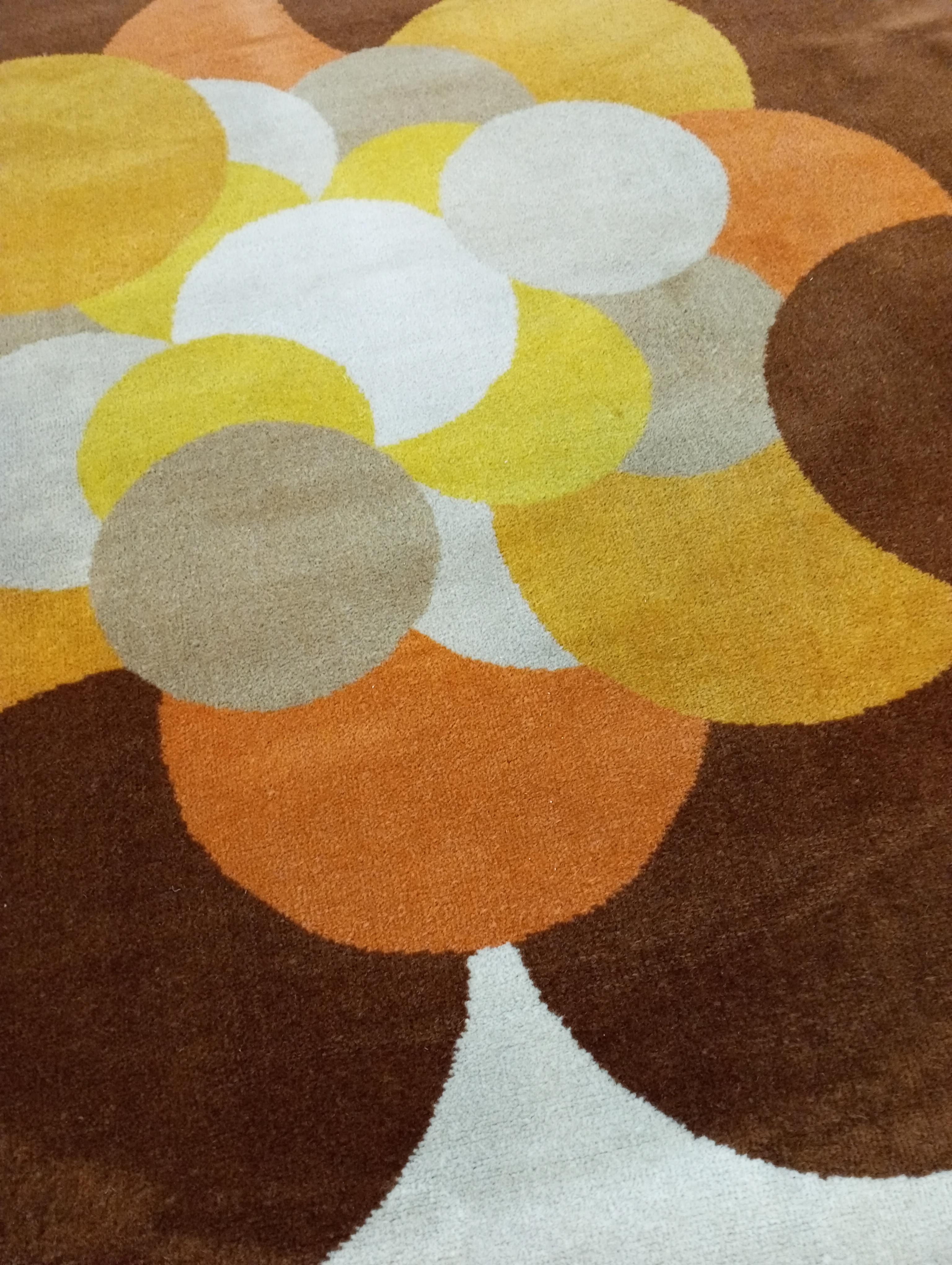 Ce tapis rond, fabriqué en Italie dans les années 1970, a un diamètre de 182 cm et est entièrement en laine. La base du tapis est d'un blanc chaud et doux, qui fait ressortir le motif géométrique des cercles  superposés, disposés dans différentes