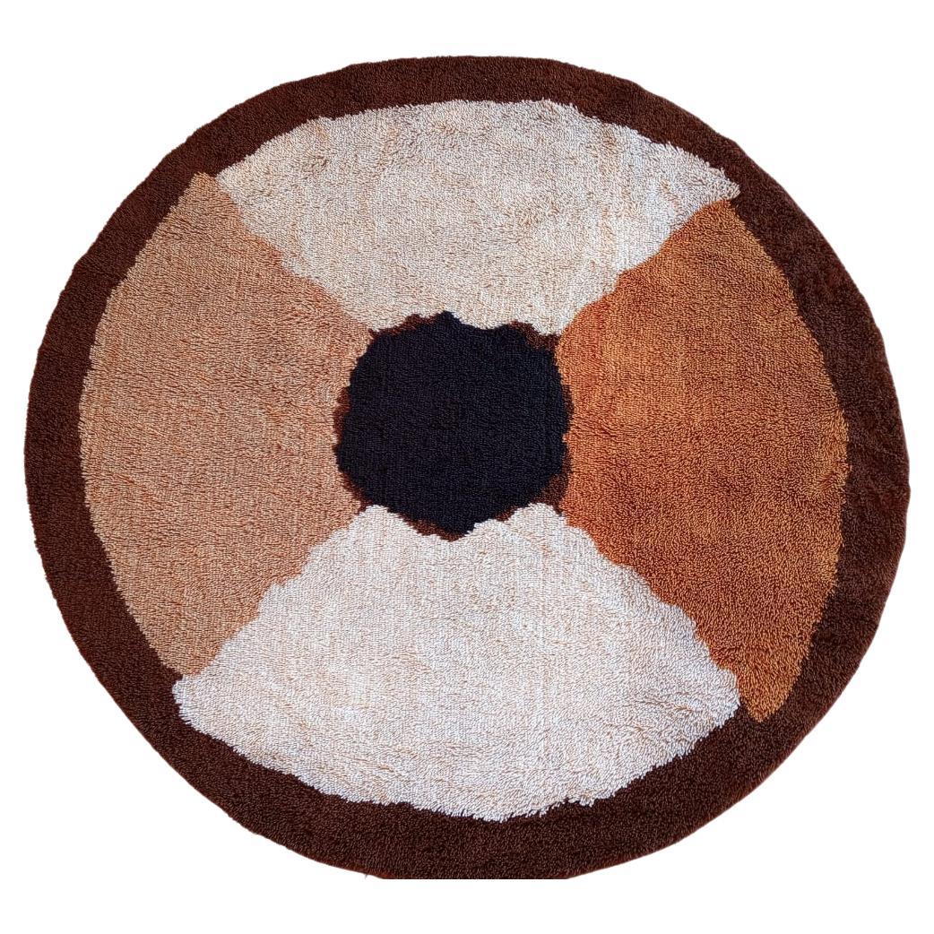 Questo tappeto a un design geometrico con colori caldi, è diviso in quattro sezioni che si incontrano in un centro nero. Ogni sezione ha una tonalità diversa bianco, beige e marrone chiaro. Il tutto è circondato da un bordo marrone scuro che