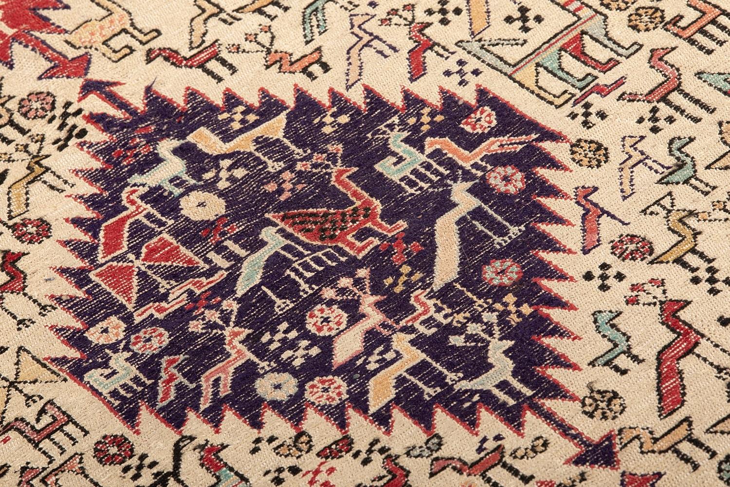 Tappeto Sumak in stile caucasico tradizionale, annodato a mano, caratterizzato da un motivo geometrico centrale con medaglioni a forma di rombo e una ricca decorazione di forme stilizzate su campo rosso e beige, incorniciato da una bordura rossa con