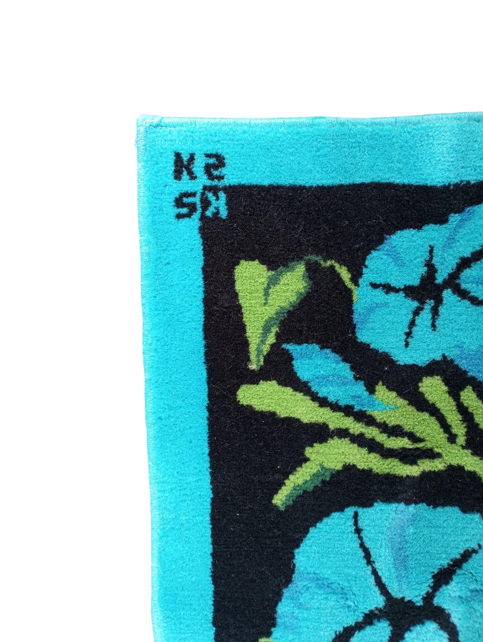 Ce tapis vintage des années 1970, réalisé par  Ken Scott (1918-1991), célèbre designer américain connu pour ses motifs floraux audacieux et vivants. Le tapis se compose d'un fond noir sur lequel sont disposées de grandes fleurs en forme de cloche