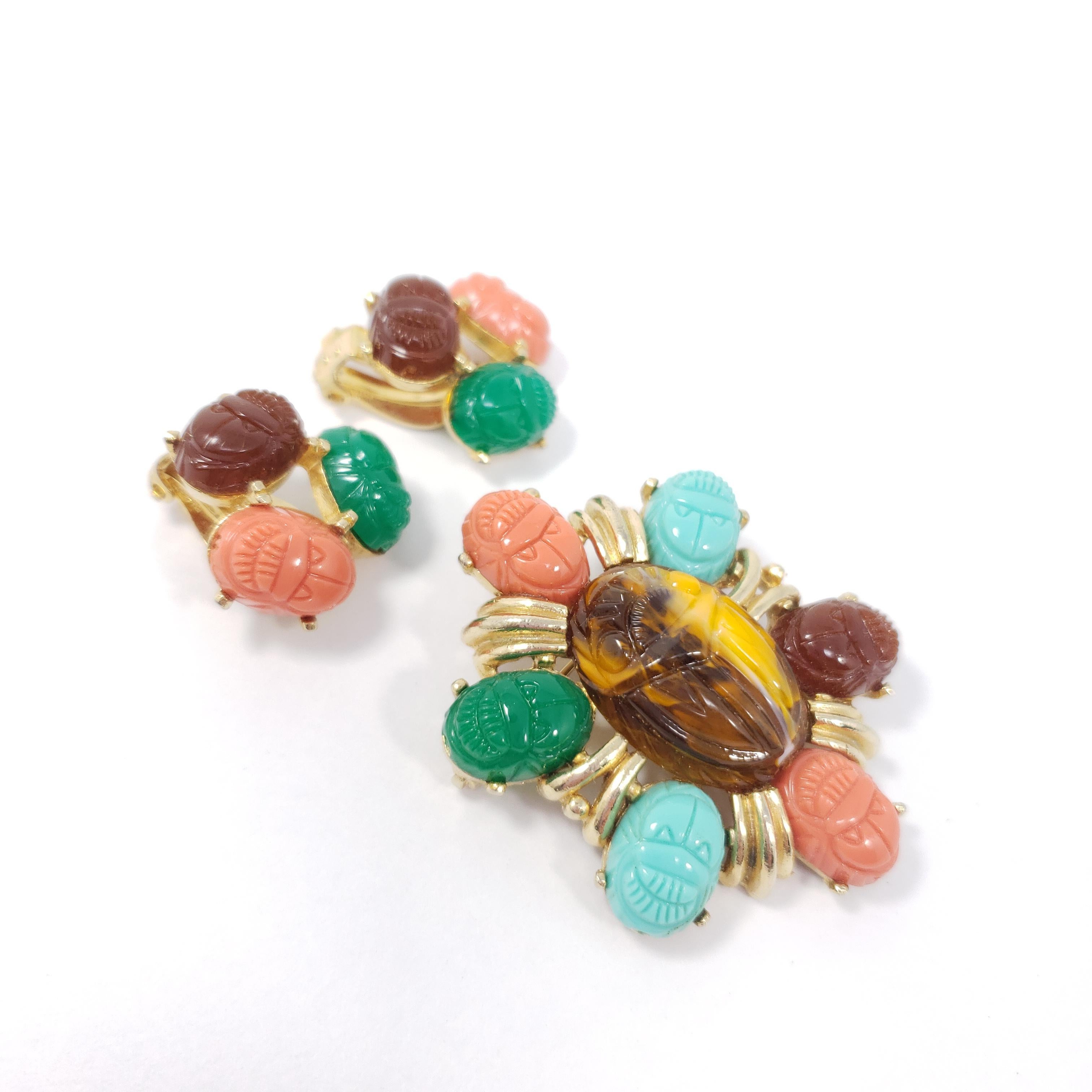 A colorful pin brooch and clip-on earring set by Tara, a mid-1900s costume jewelry designer. Each piece features colorful carved resin scarabs prong-set in a gold-tone metal setting. DeLizza and Elster are believed to be the original designers