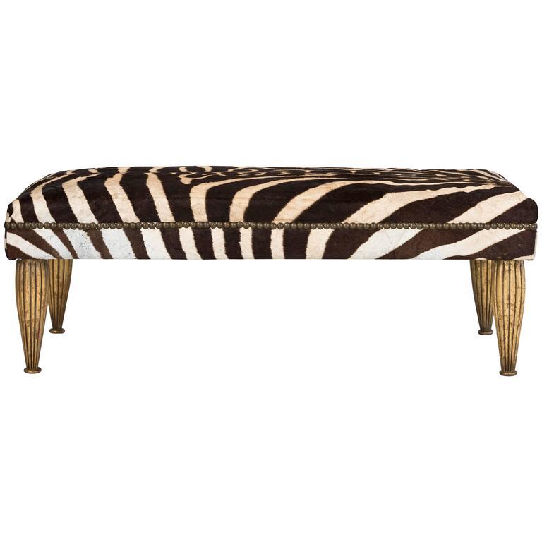 This elegant upholstered bench with gold leaf or gilded legs and nailhead trim is part of the custom Tara Shaw Maison collection. Handcrafted in New Orleans. Standard bench available upholstered in white cowhide, zebra hide or heavyweight Belgian