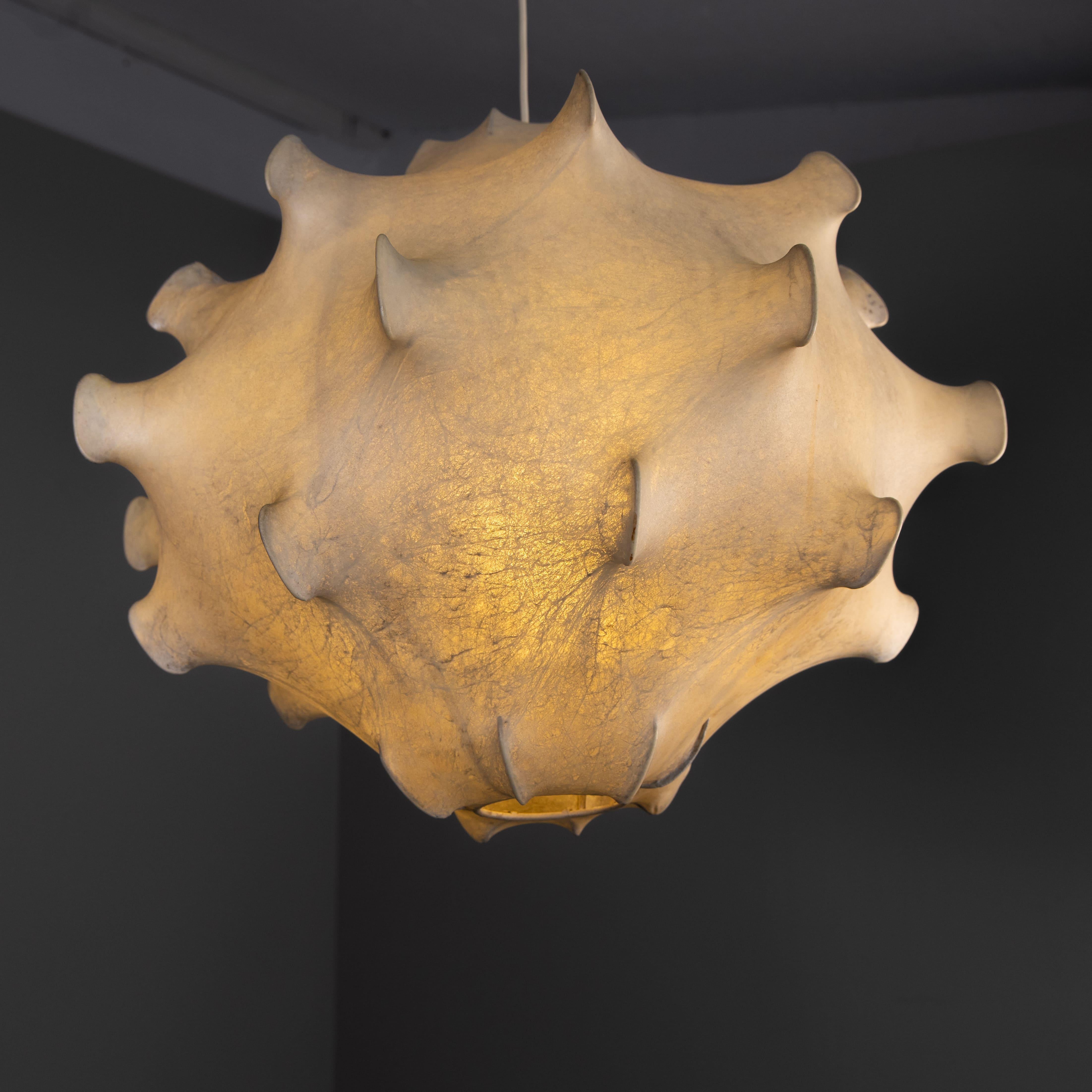 Questa iconica lampada a sospensione Cocoon Taraxacum è stata progettata da Achille e Pier Giacomo Castiglioni per Flos Italia negli anni Sessanta. Presenta una struttura interna in acciaio con una presa E27 ed è ricoperta da una copertura in resina