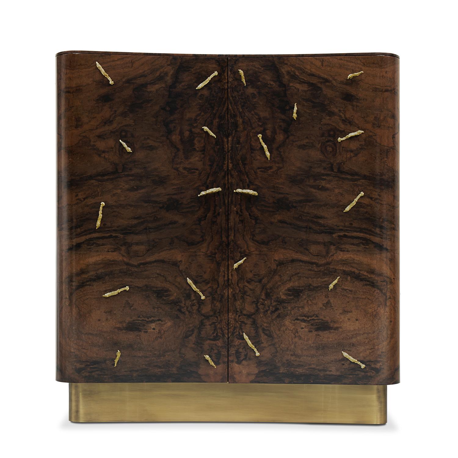 Armario Cómoda Tarius Alto con estructura de madera de nogal maciza
chapa de madera en acabado mate. Con detalles de latón macizo pulido y con
Base de latón envejecido cepillado. Con 2 puertas, 1 estante de cristal transparente y con 
4 cajones